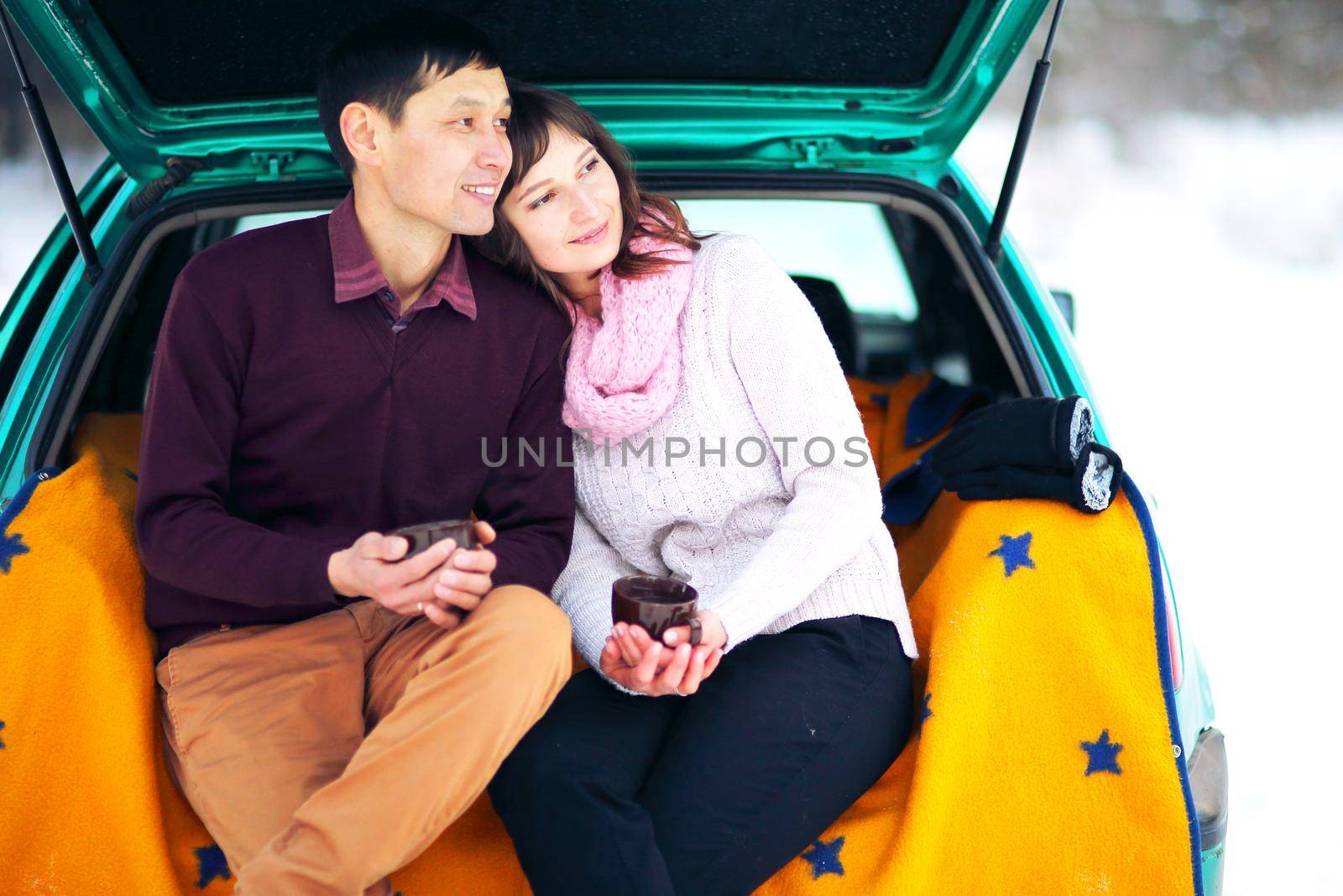 Happy couple sitting in the open trunk of a car in winter on nature by selinsmo