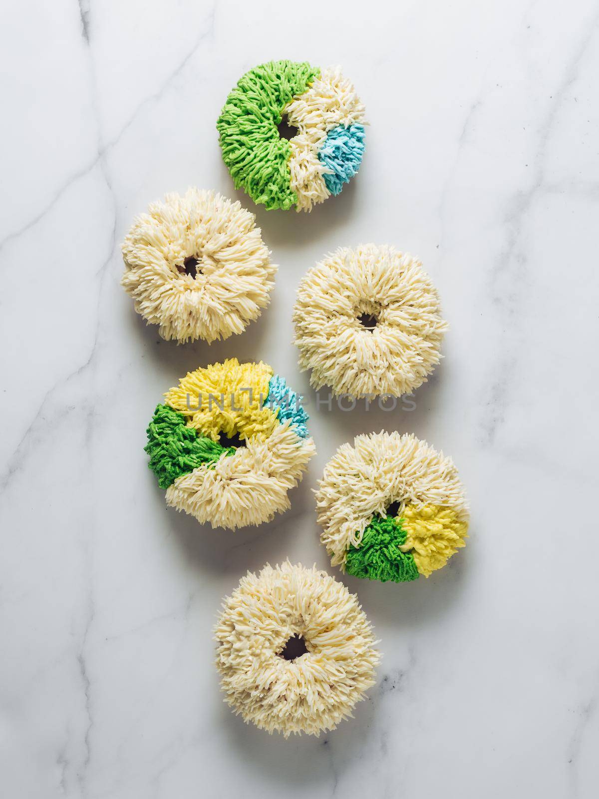 Shag donuts on white marble background. Unusual trendy colorful donuts with vanilla buttercream. Copy space. Top view or flat lay. Vertical