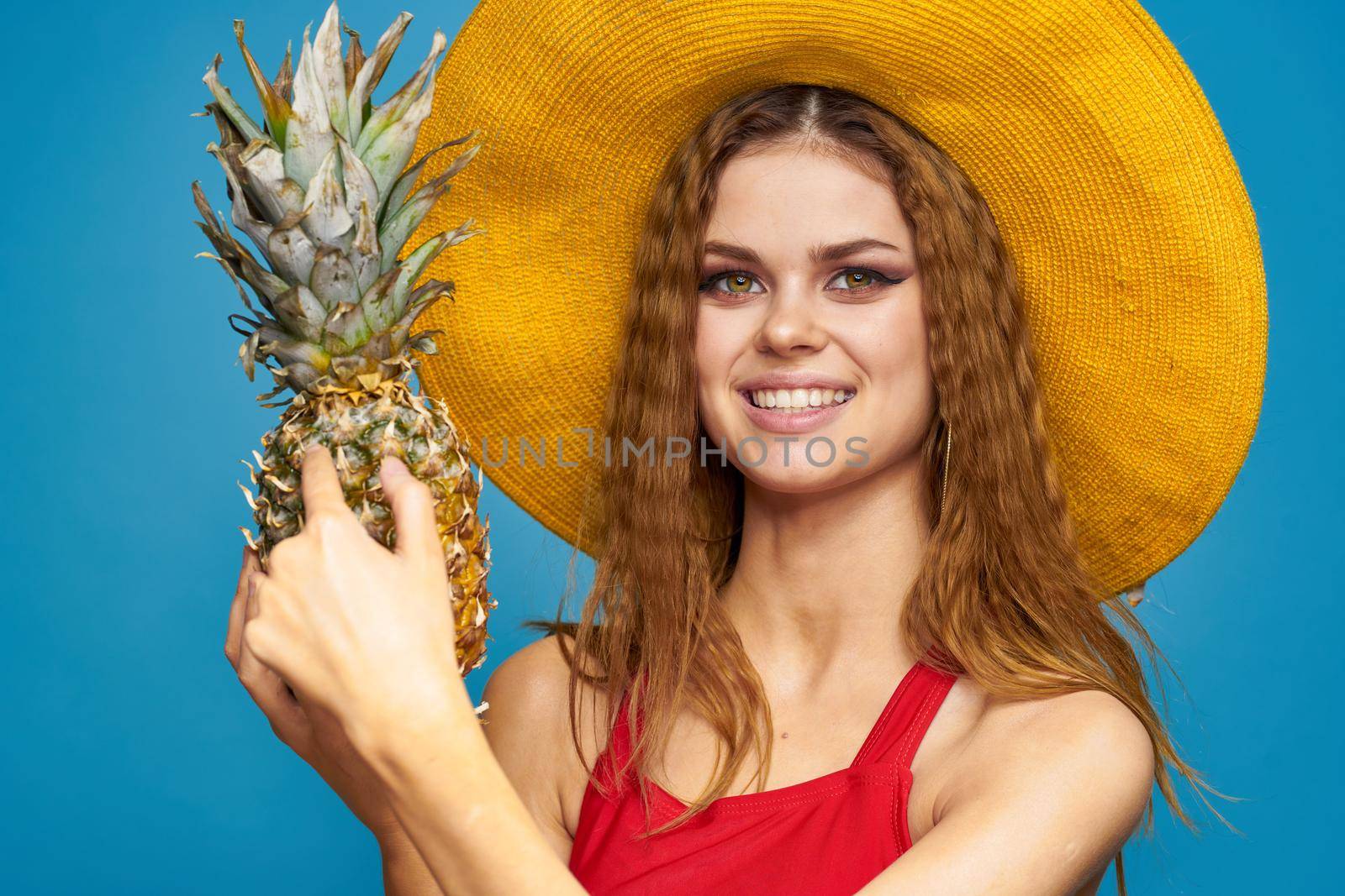 Woman in yellow hat with pineapple in hands emotions fun lifestyle summer fruit blue background. High quality photo