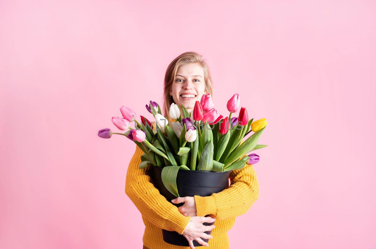 Women's Day or Mother's Day celebration. Happy young woman holding bucket of fresh tulips isolated on pink background