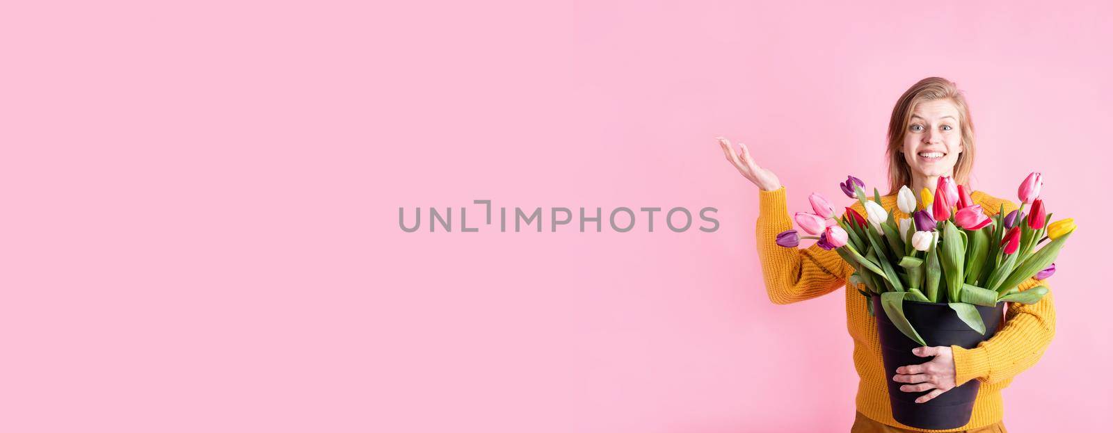 Women's Day or Mother's Day celebration. Banner. Happy young woman holding bucket of fresh tulips isolated on pink background