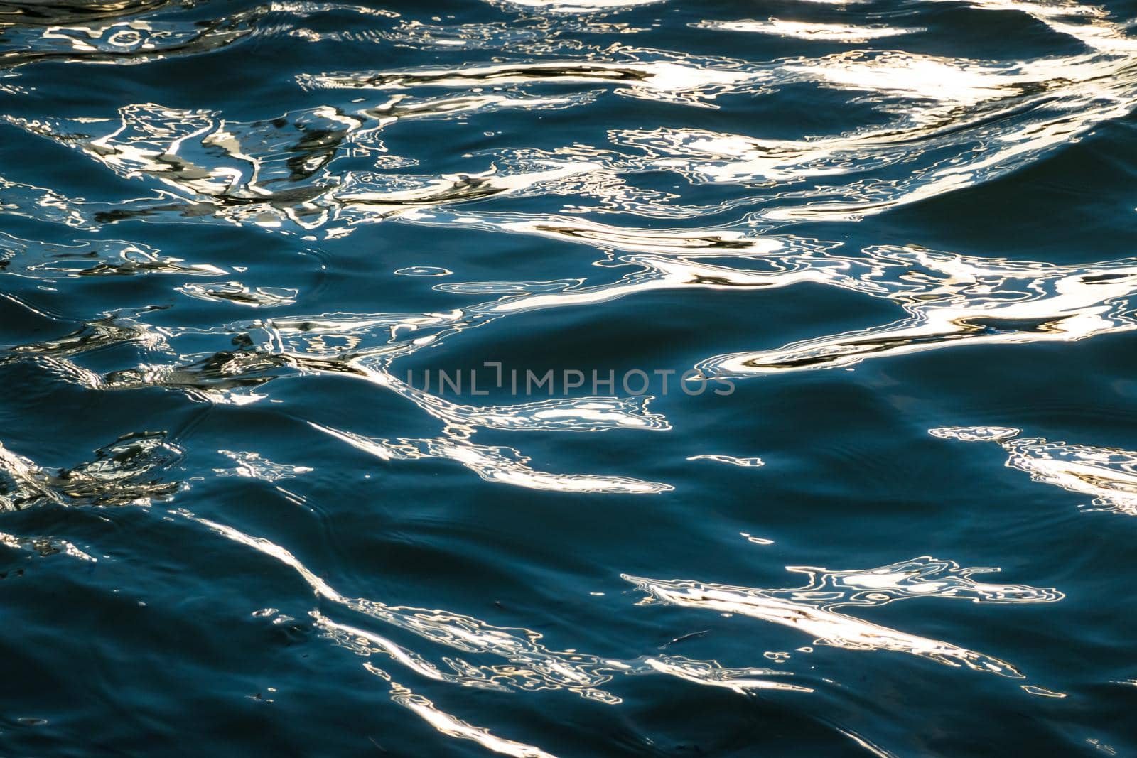 Dark blue rippled water surface background with bright golden sunlight reflection