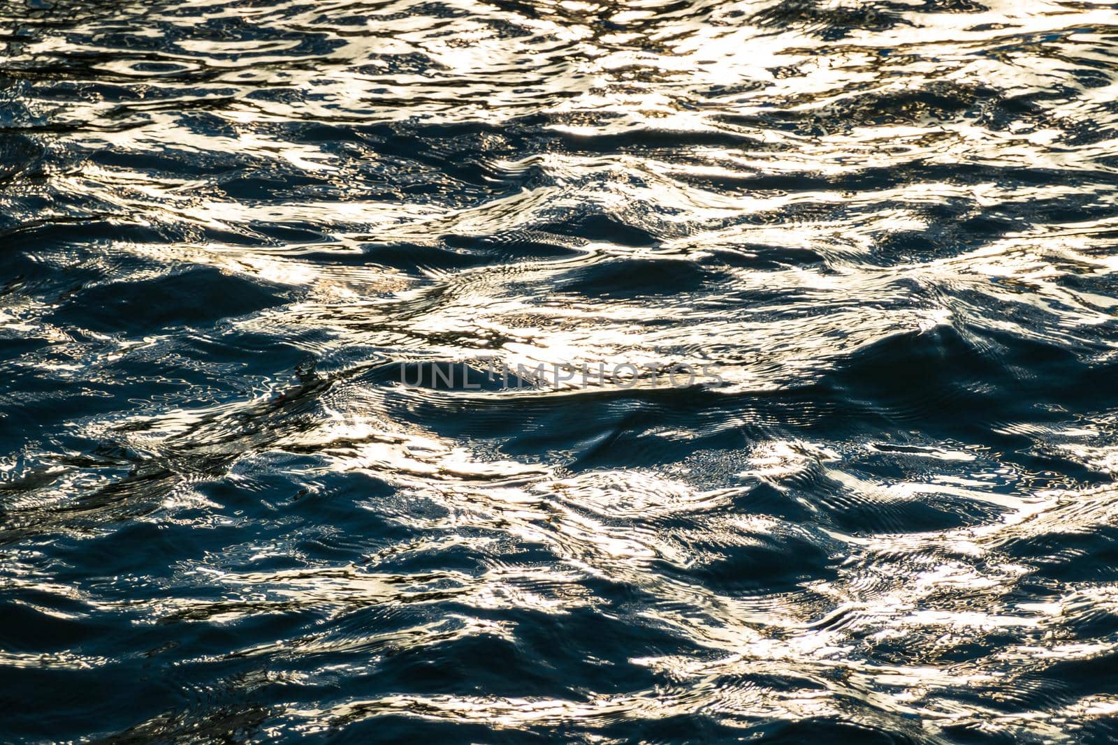 Dark rippled water surface background with bright golden sunlight reflection