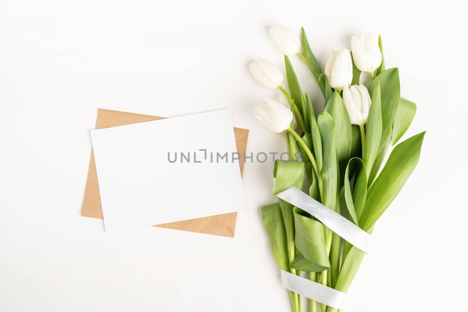 Mock up design. Fresh cut white tulip flowers and blank card with envelope top view on white background with copy space