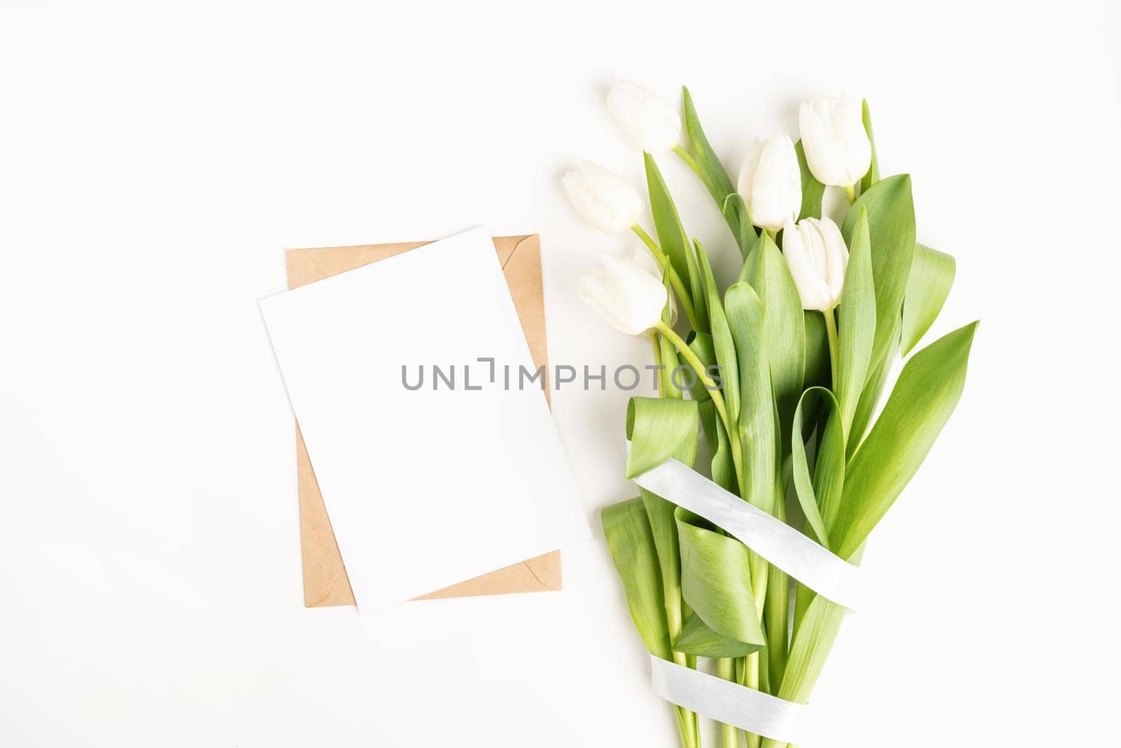 Mock up design. Fresh cut white tulip flowers and blank card with envelope top view on white background with copy space