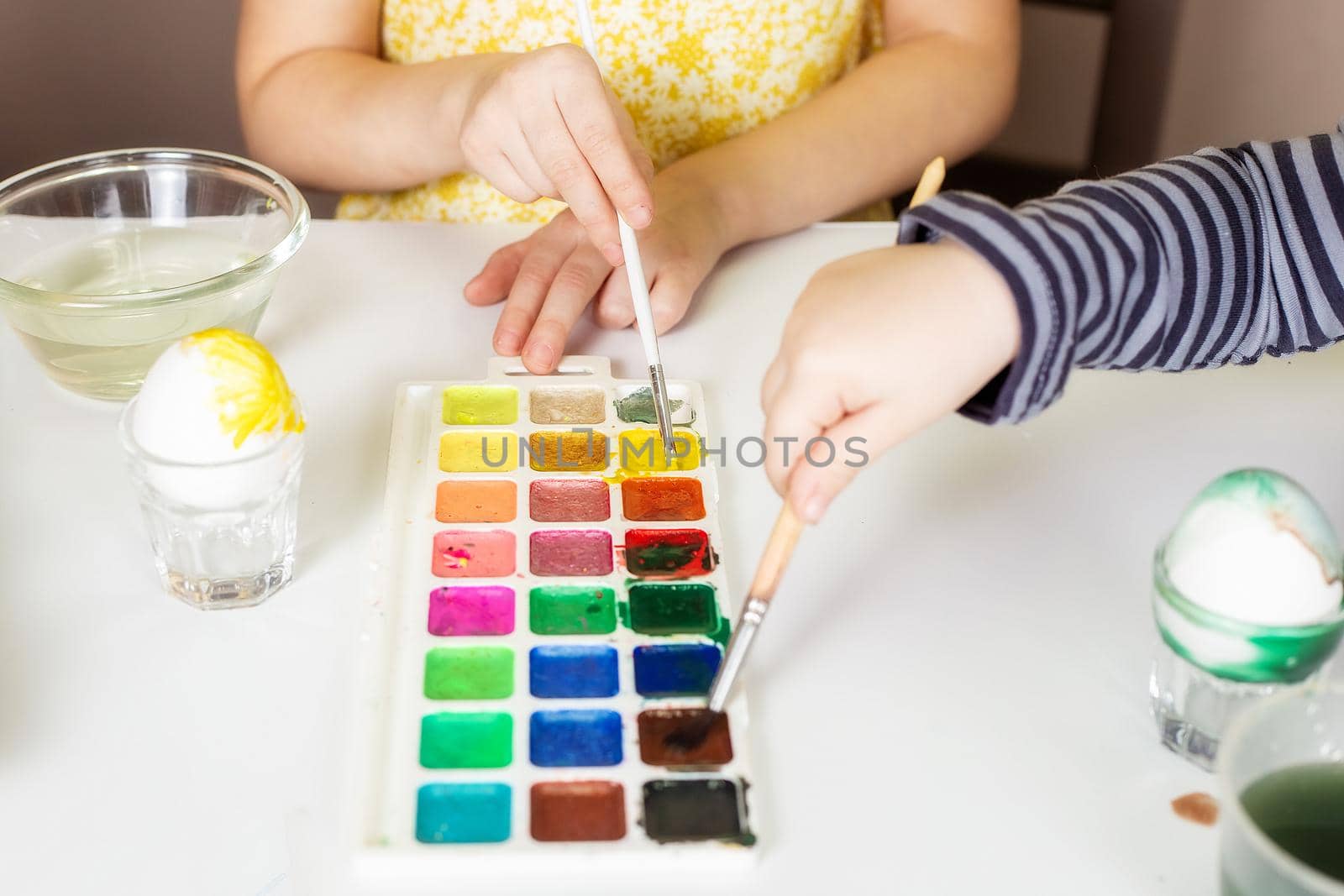 Close-up on the hands of little Caucasian children who paint eggs with special paints for the Christian spring holiday of Easter.