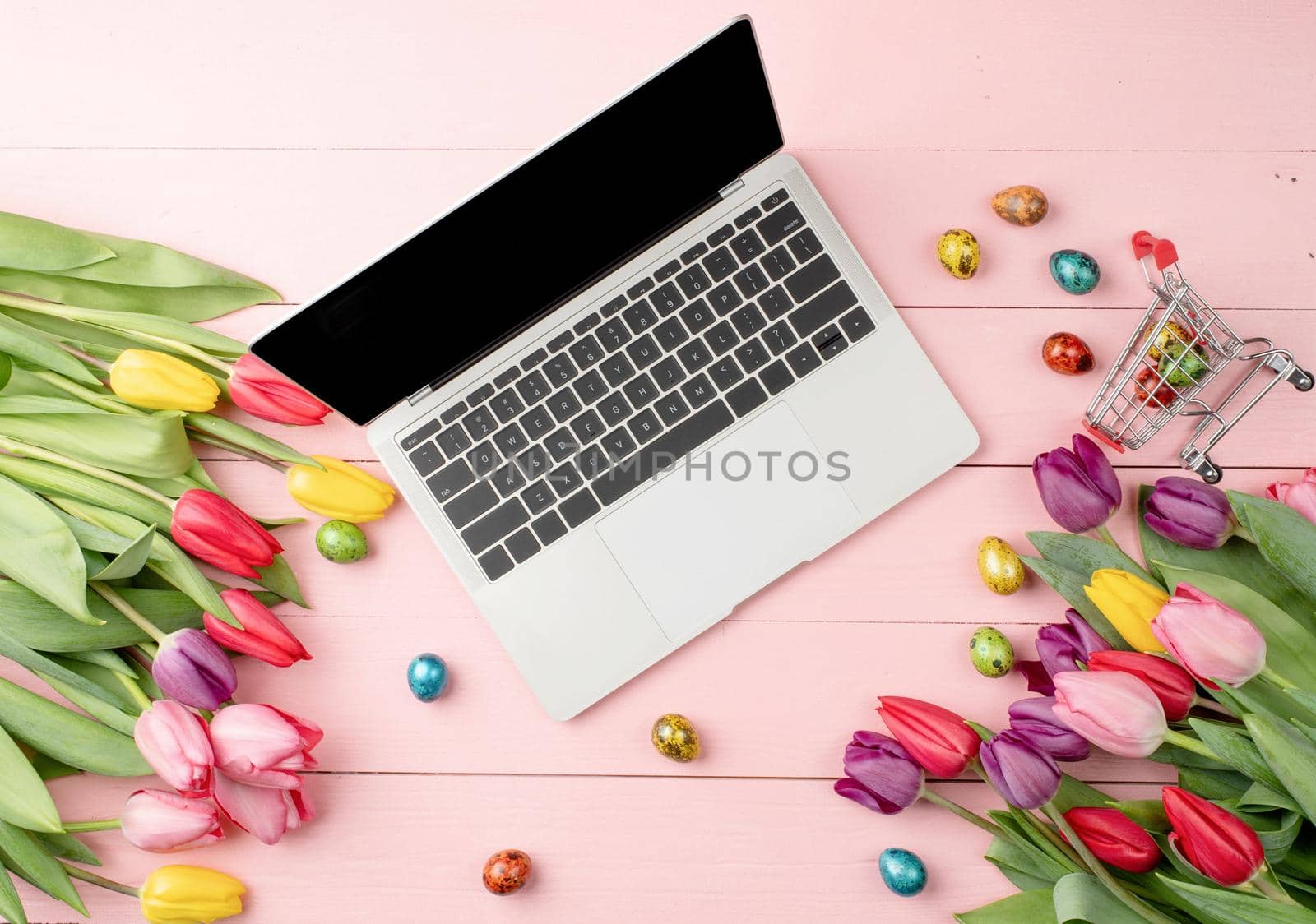 Easter and spring concept. Top view of laptop computer, colorful tulips and Easter eggs on pink wooden background