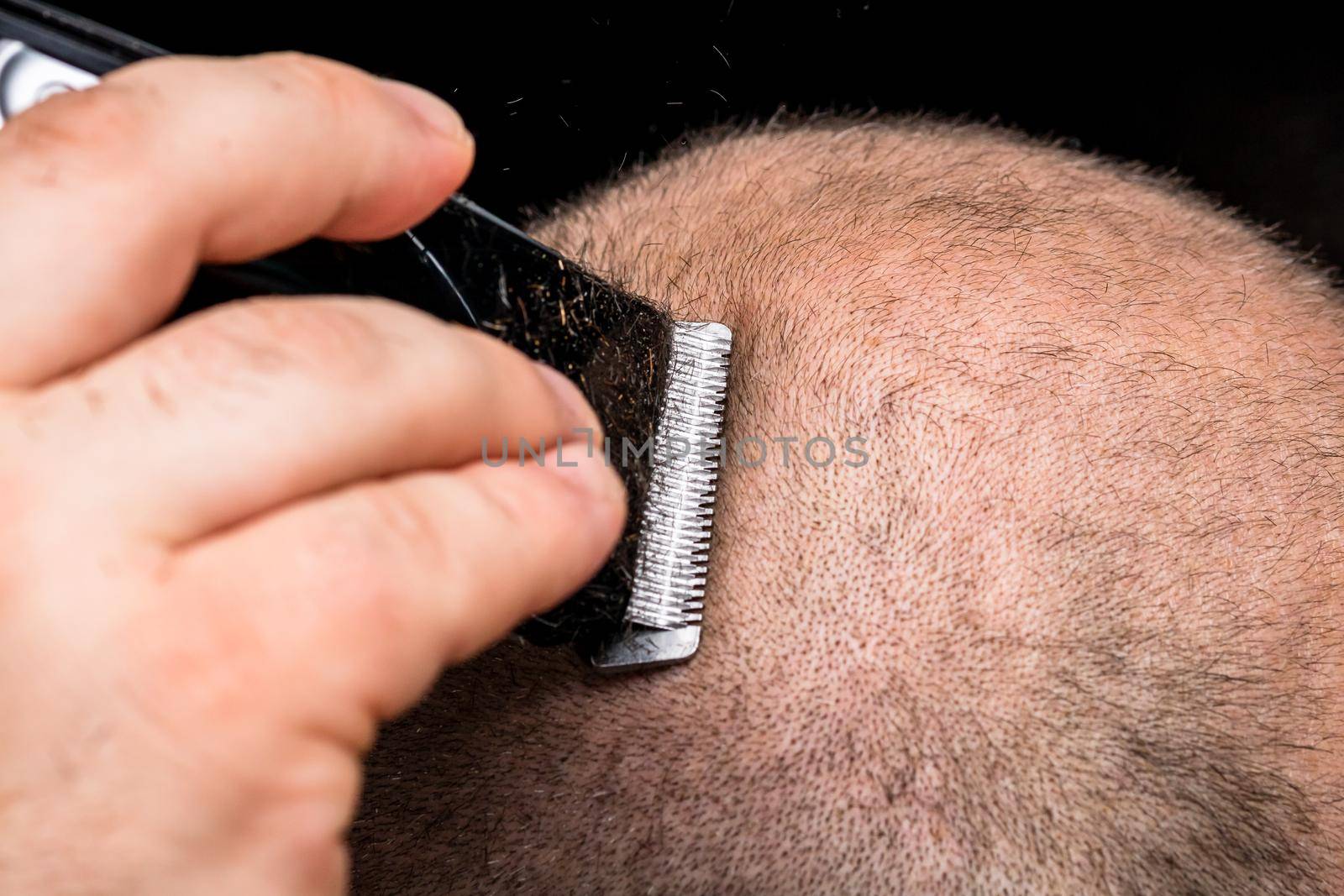 Man shaving or trimming his hair using a hair clipper by vladispas