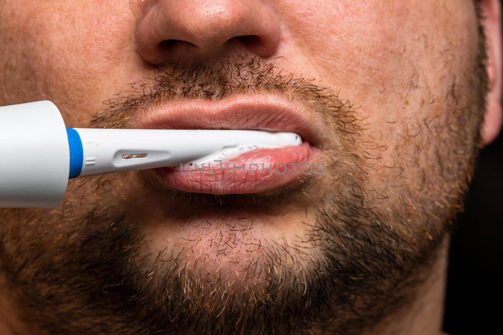 Close up of man brushing his teeth with electric toothbrush by vladispas