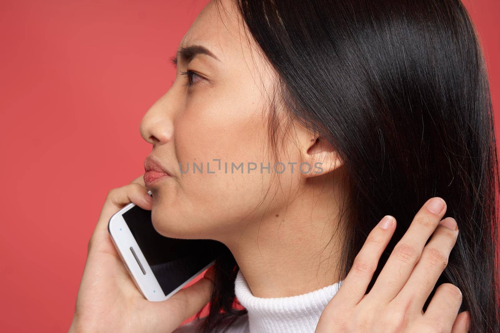 woman of asian appearance talking on the phone emotions dissatisfaction close-up red background. High quality photo