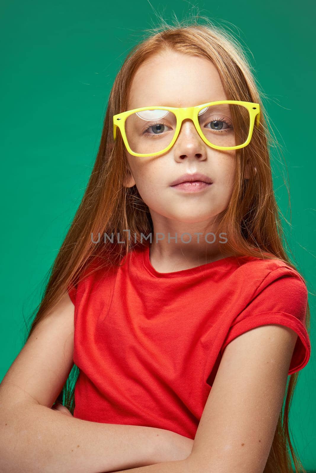 cute red-haired girl with glasses gesturing with her hands school childhood green background. High quality photo