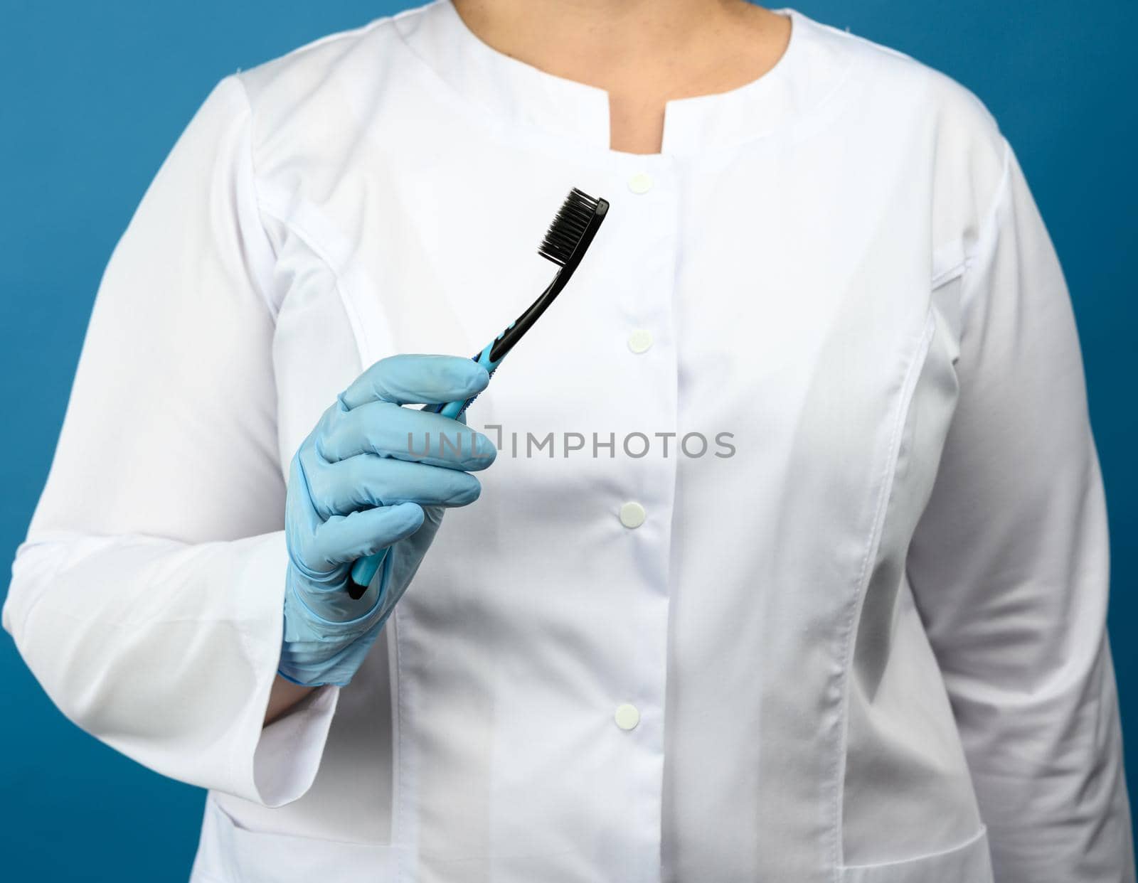 doctor in a white medical coat and mask stands on a blue background and holds a plastic toothbrush by ndanko