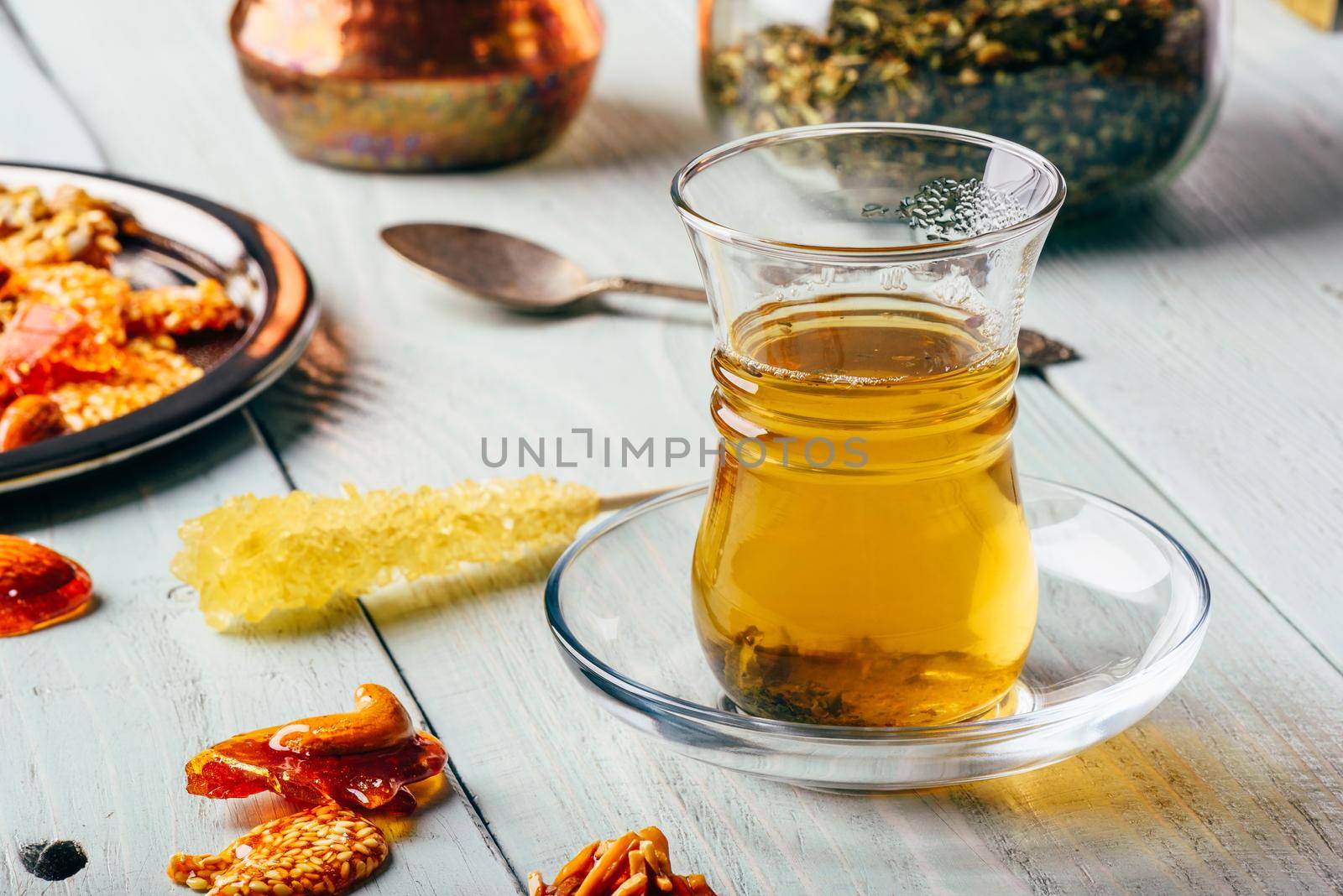 Herbal tea in oriental glass with arabian nut delights on metal plate over light wooden surface