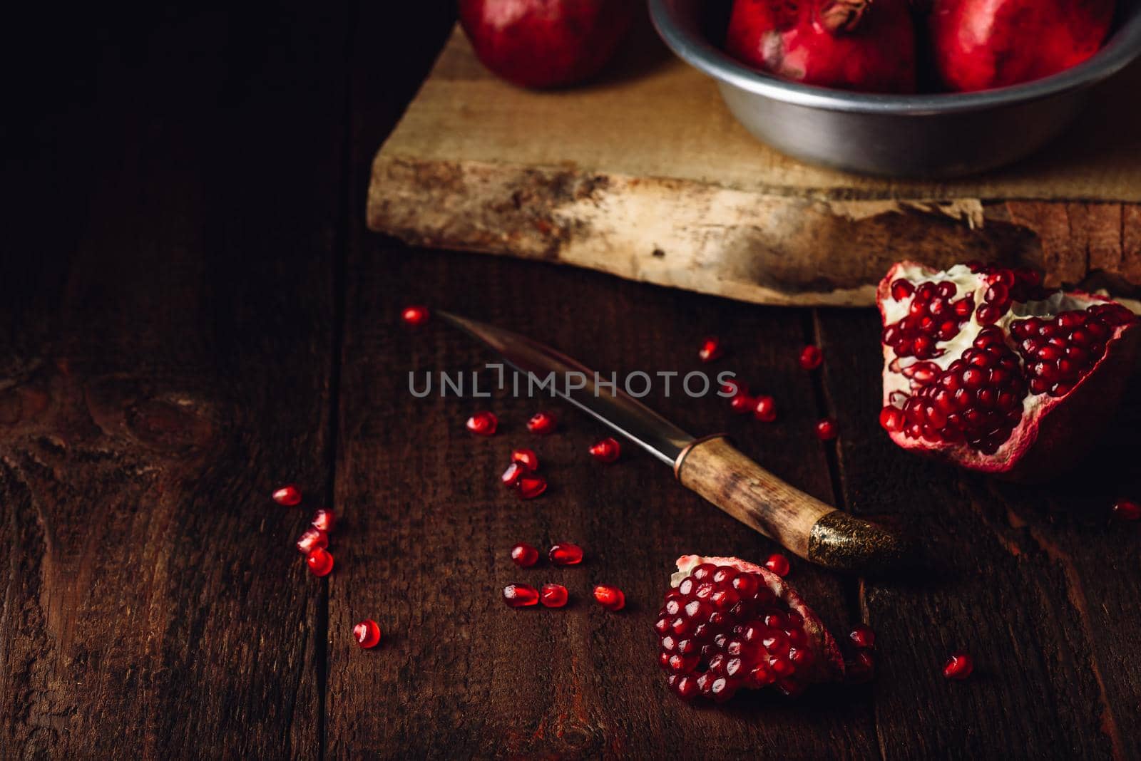 Pomegranate fruits with knife on rustic wooden surface.
