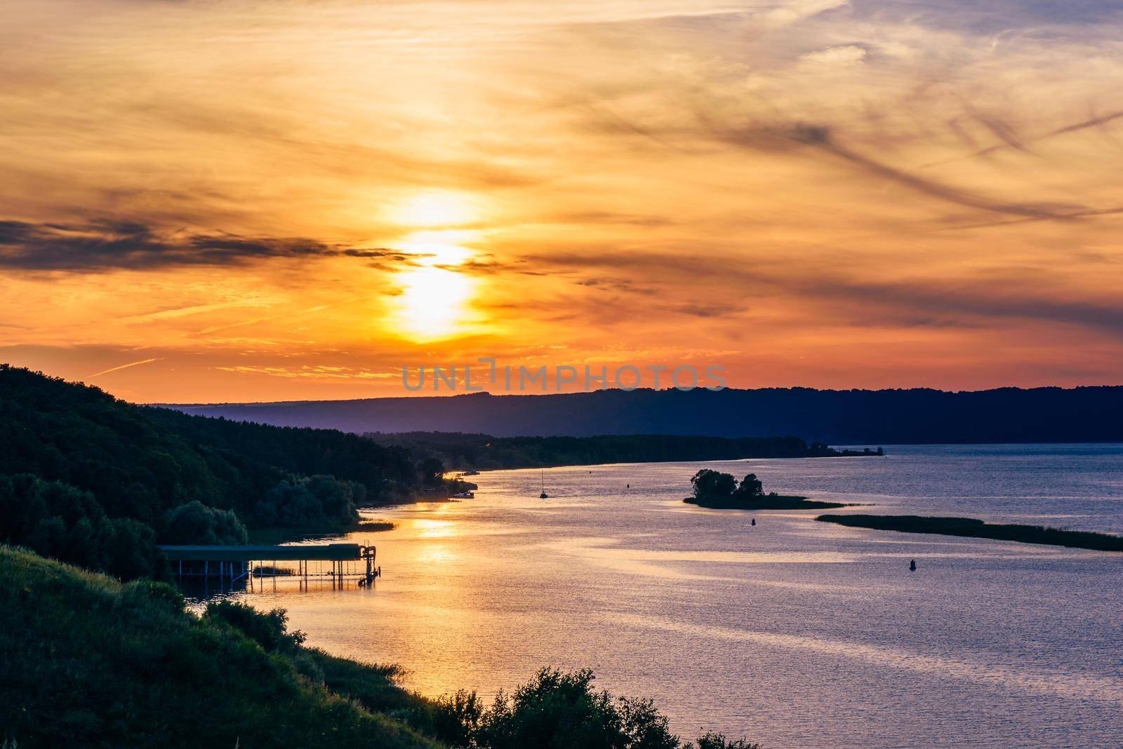 Summer sunset over the river shore with sky reflected on water