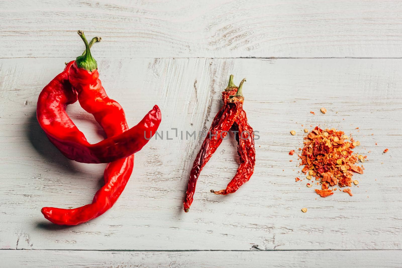 Fresh, dried and crushed red chili pepper over colored wooden background