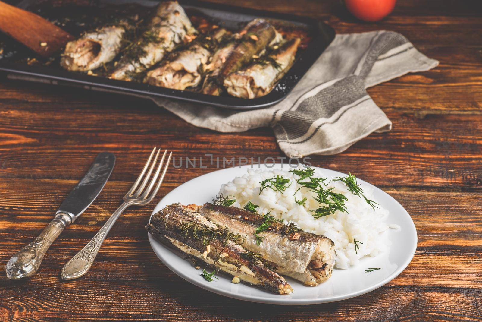 Baked hake carcasses with rice on white plate