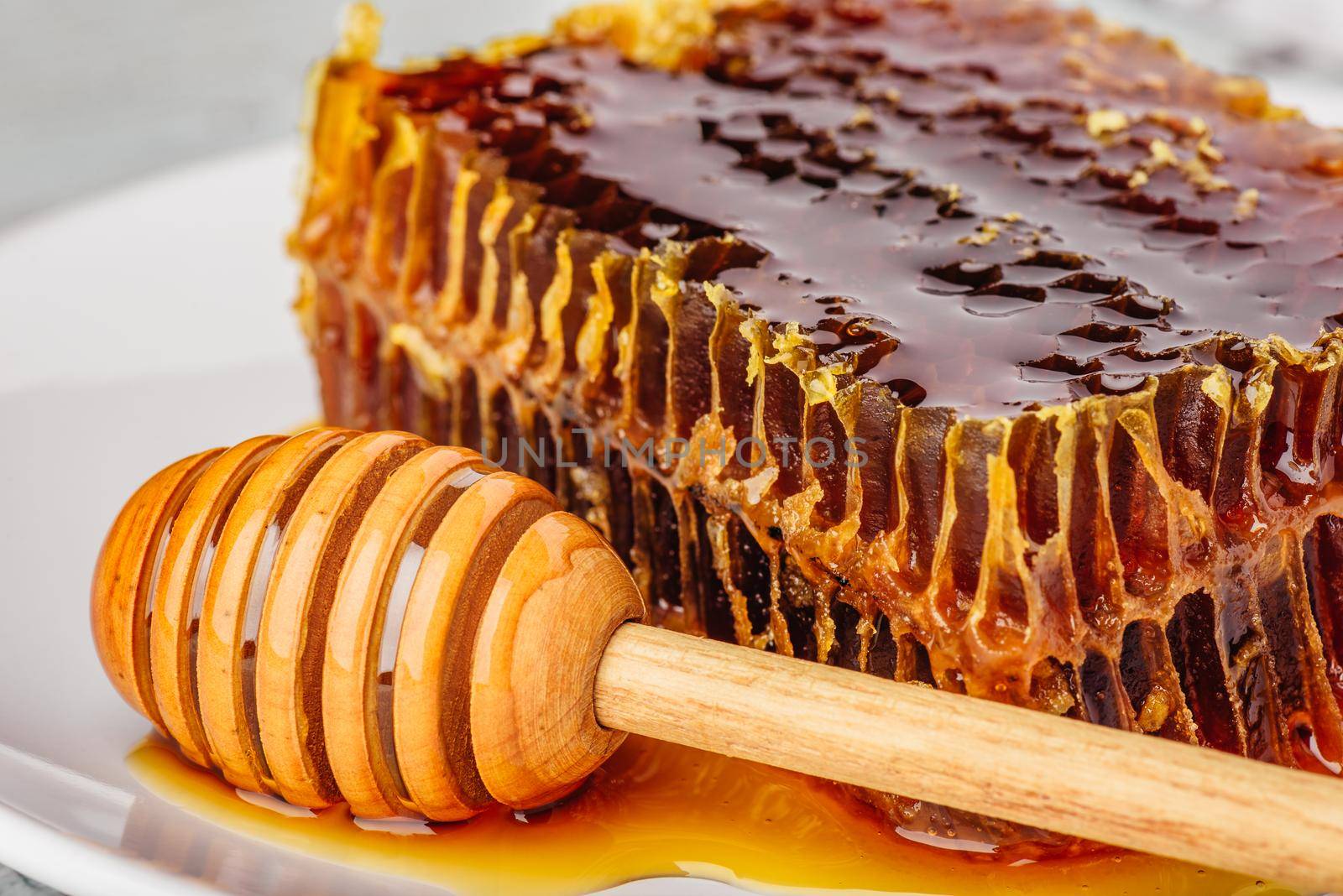 Delicious honeycomb on white plate with wooden honey dipper