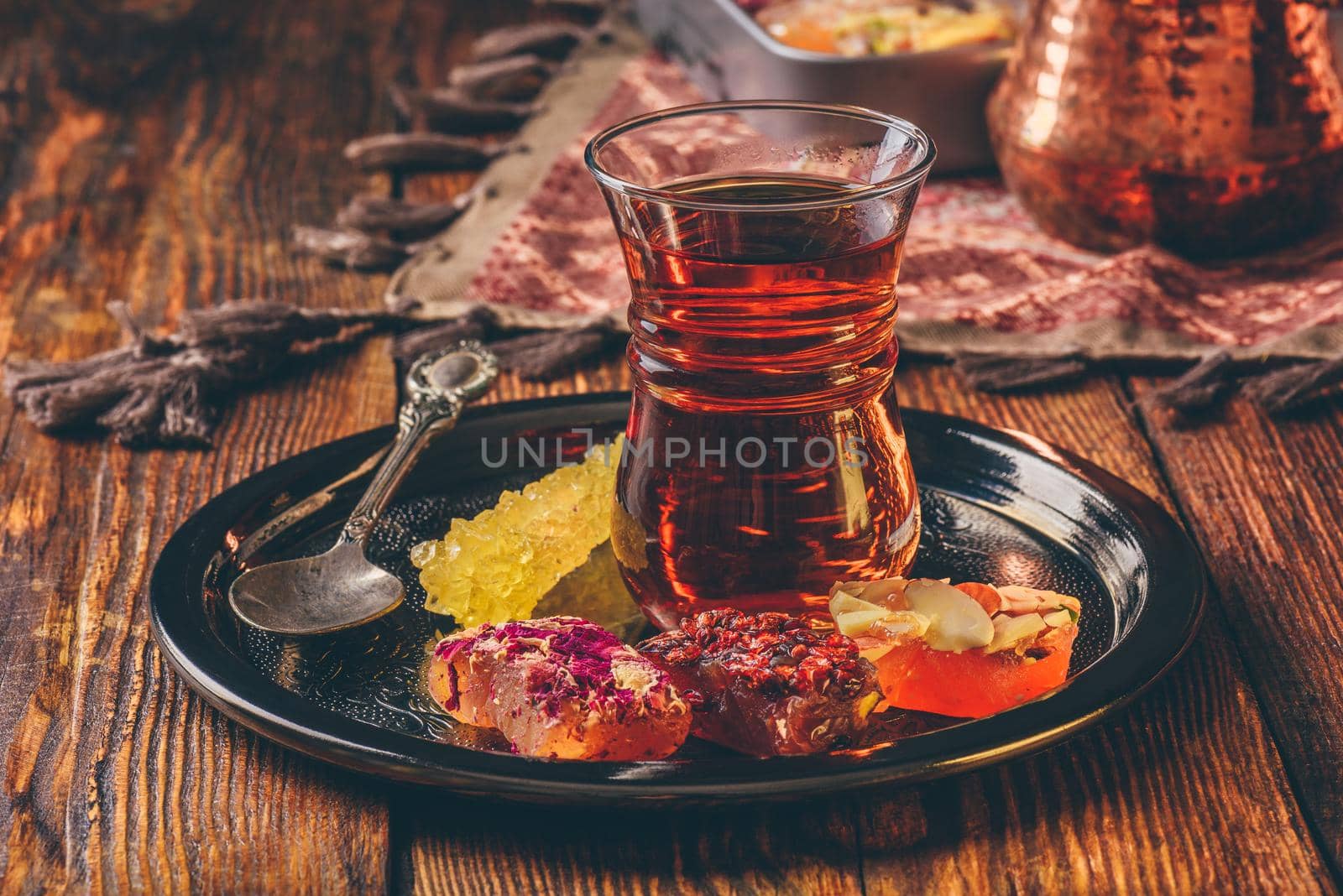 Tea in armudu glass with oriental delight rahat lokum on metal tray over wooden surface and tablecloth