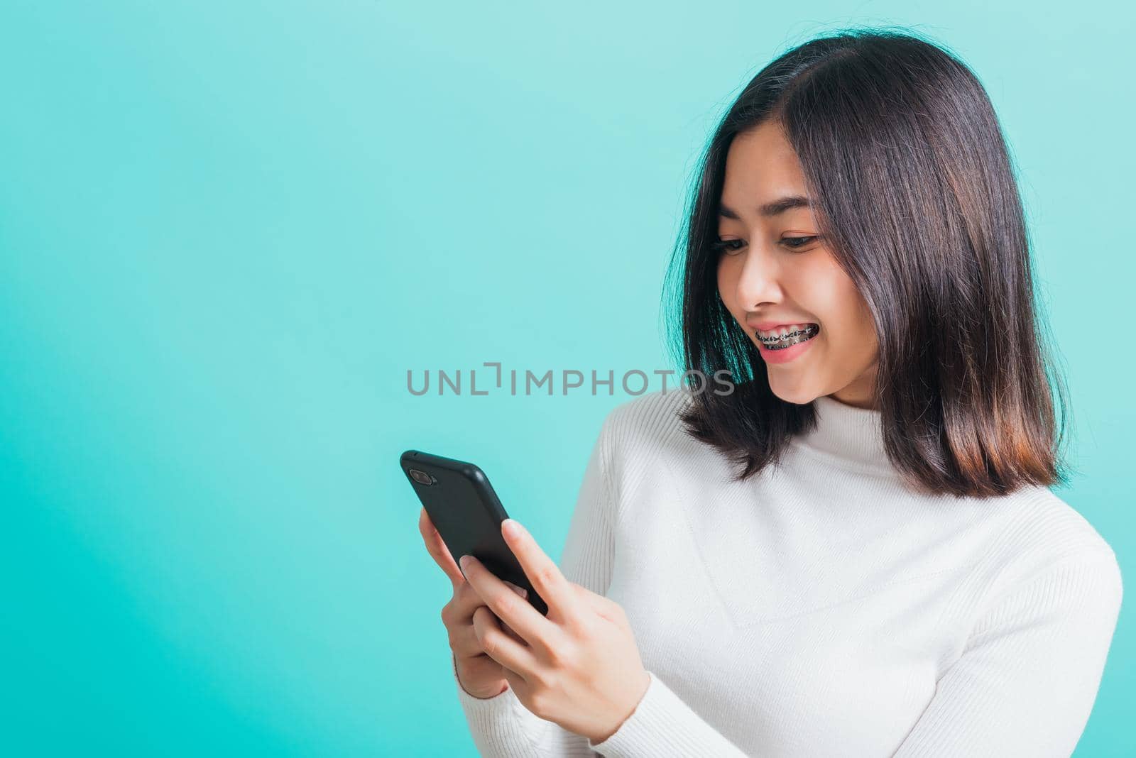 Portrait of Asian woman smile she holding and typing text message on a smartphone, female excited cheerful her reading mobile phone some social media isolated on a blue background, Technology concept