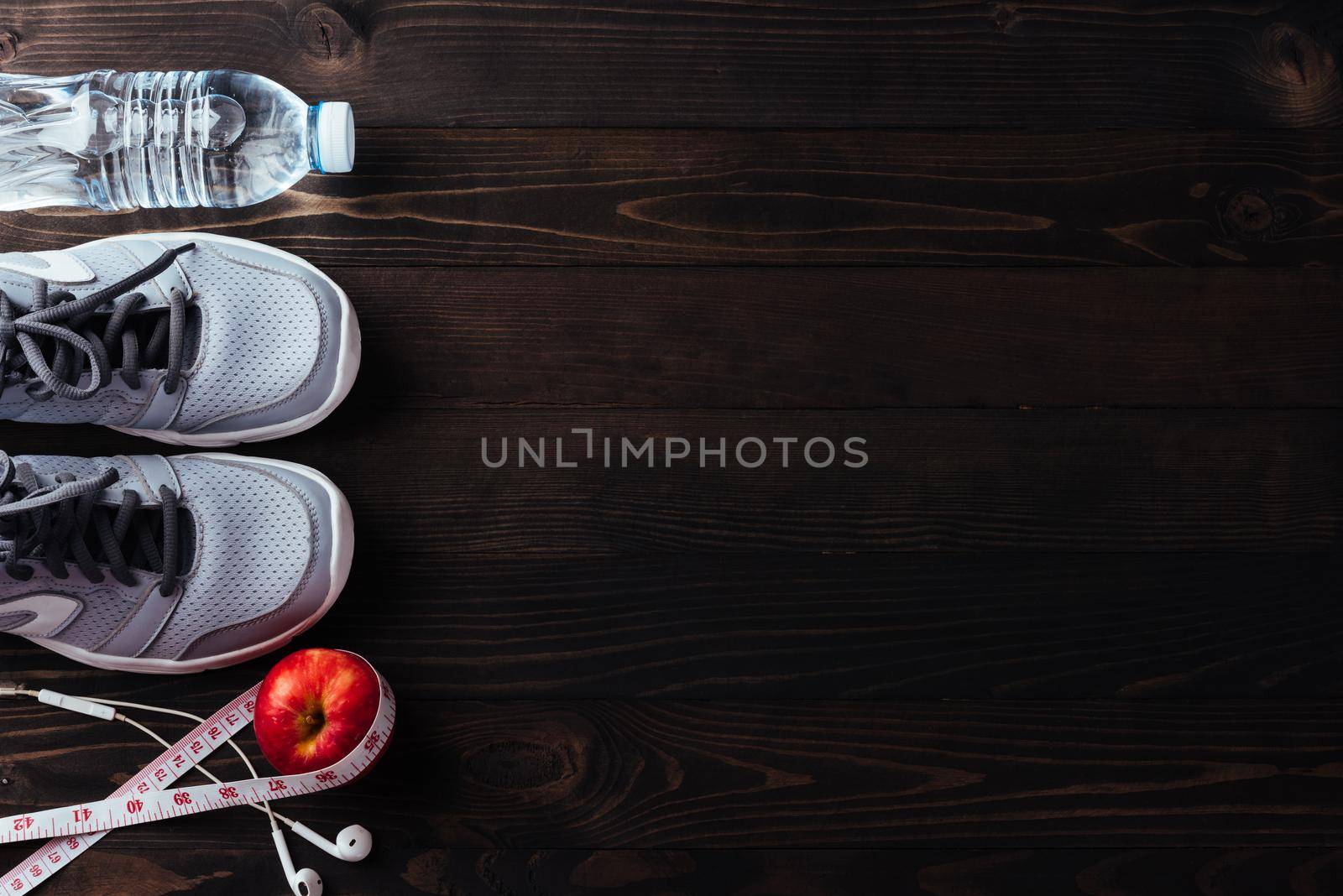 Pair sports shoes, headphones, apple and water bottle on black wood by Sorapop