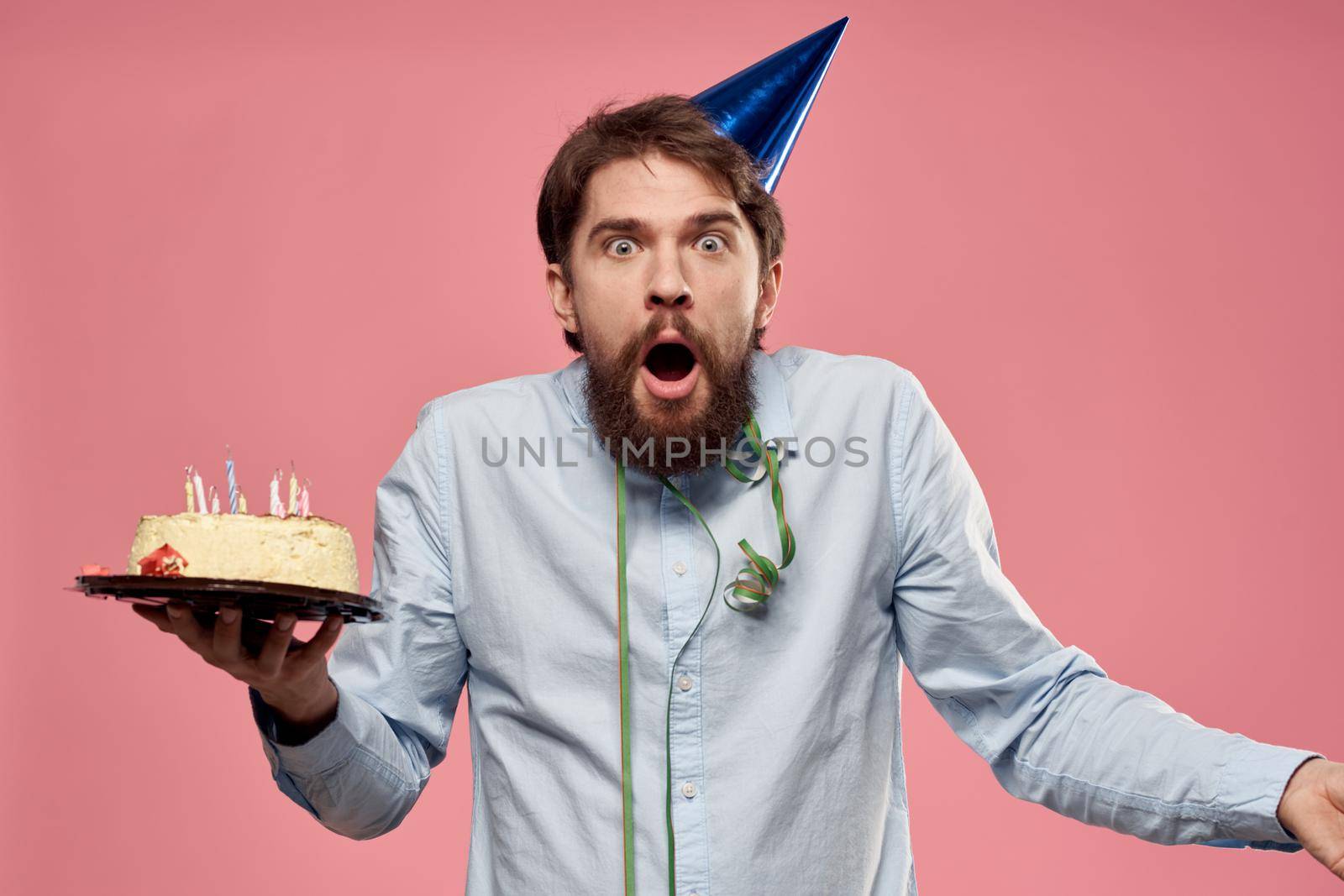 Bearded man with cake tongue on a pink background cropped view and a blue cap on his head. High quality photo