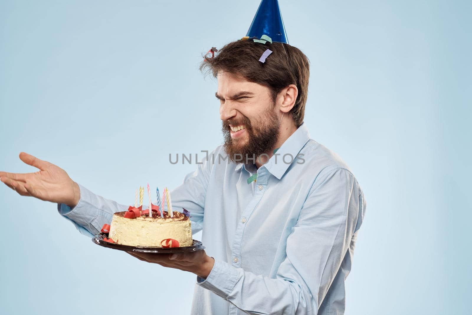 Man with a plate of cake and a festive candle blue background cap corporate party by SHOTPRIME