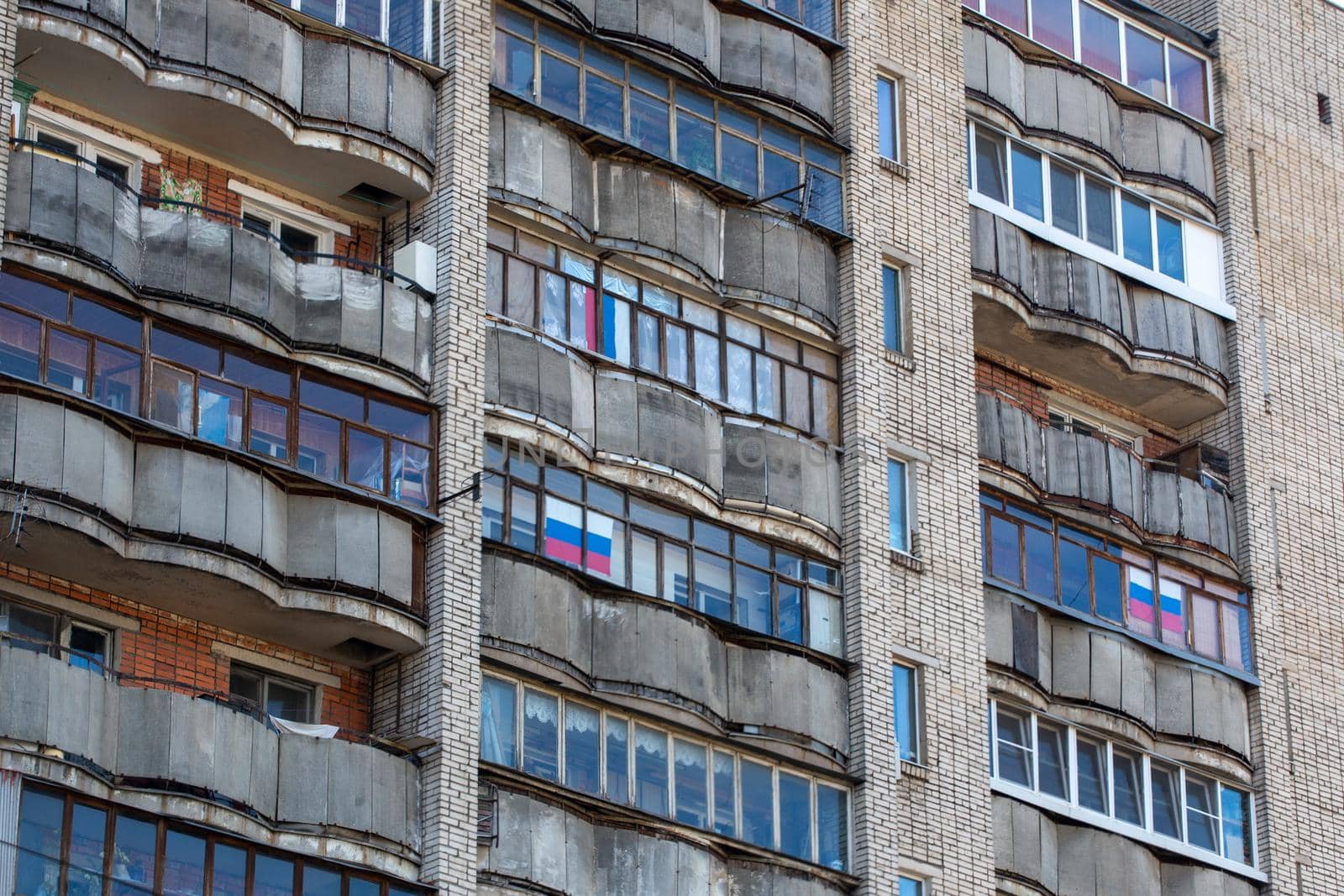 old dirty large russian apartment building balcony windows with russian tricolor flags