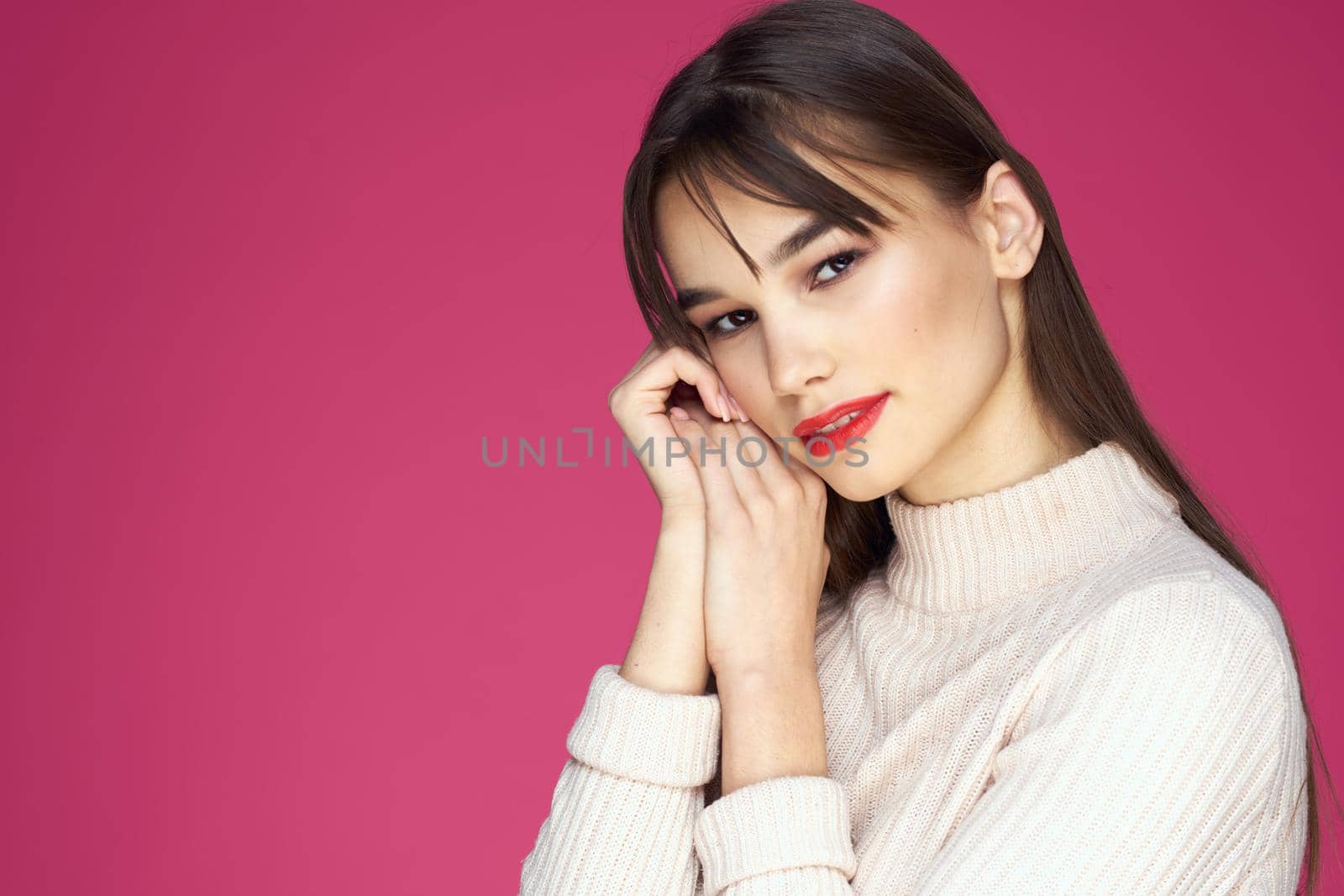 Brunette with long hair red lips cosmetics white sweater pink background cropped view. High quality photo