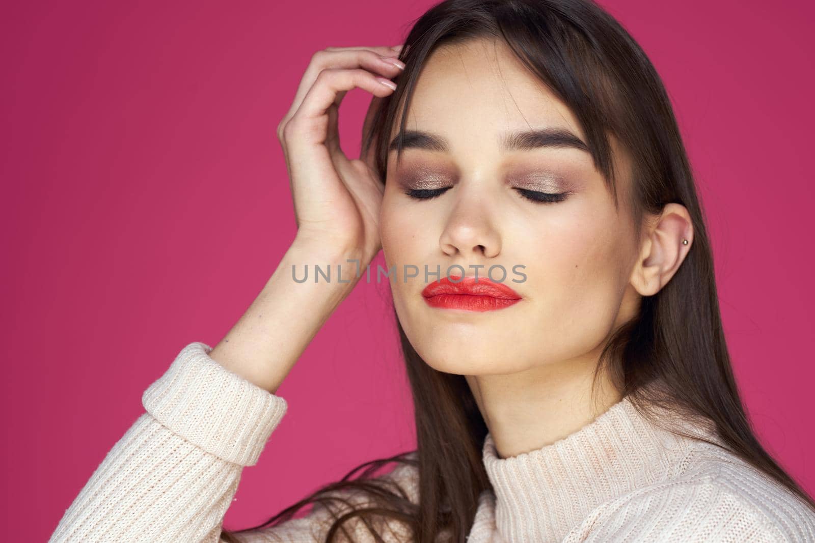 Brunette with long hair red lips cosmetics white sweater pink background cropped view. High quality photo