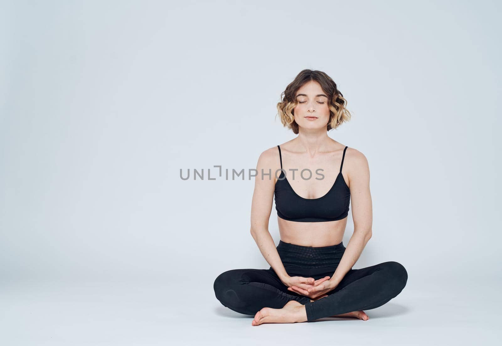 A woman is meditating on a light background with her legs crossed on the floor by SHOTPRIME