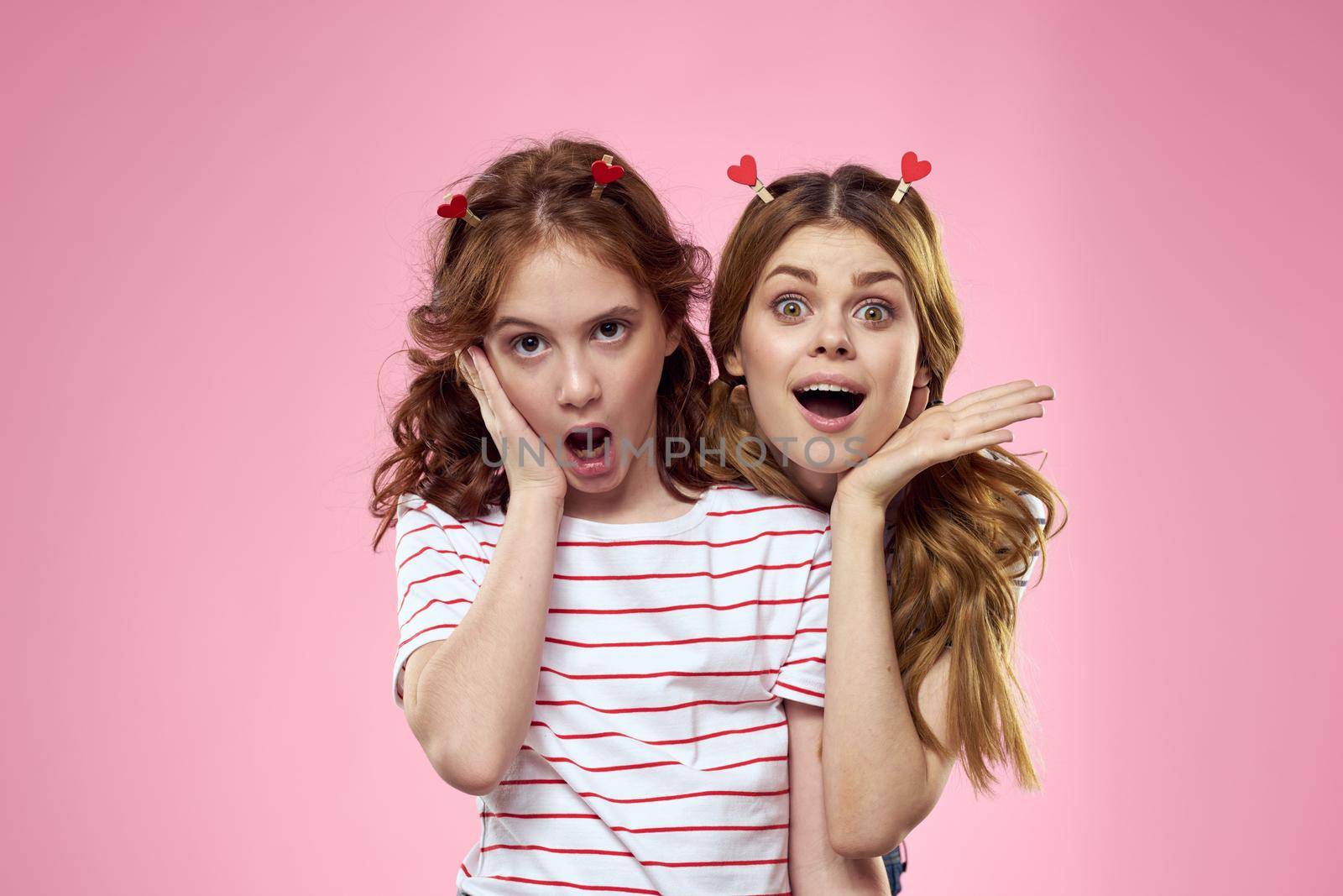 Happy sisters are having fun on a pink background and heart-shaped clothespins on their heads. High quality photo