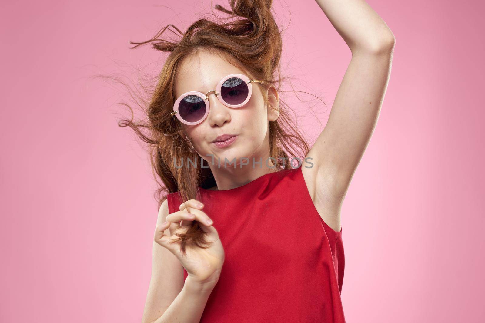 Girl with curly hair dark round glasses fun red dress pink background. High quality photo
