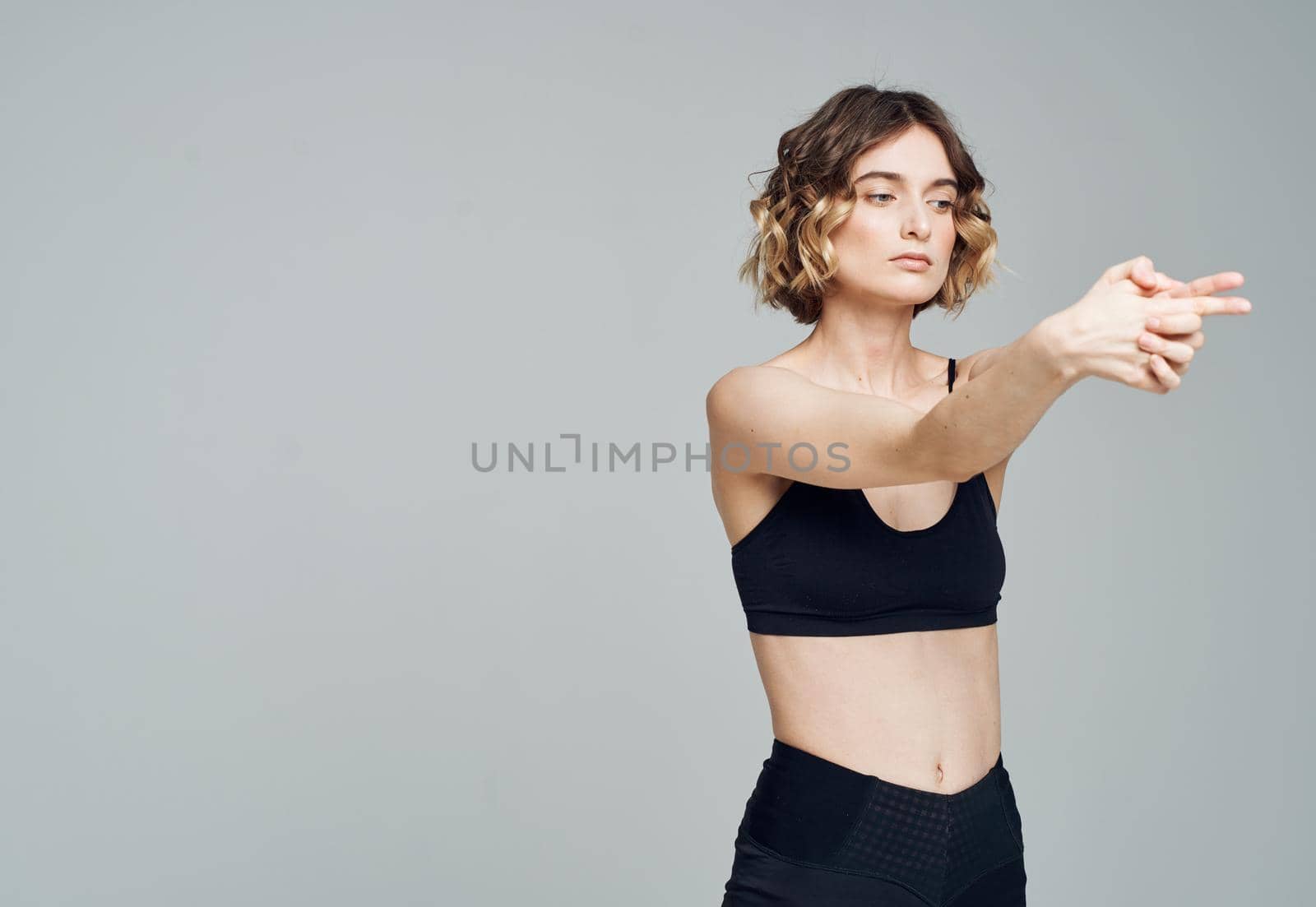 A woman in dark sportswear on a gray background gestures with her hands. High quality photo