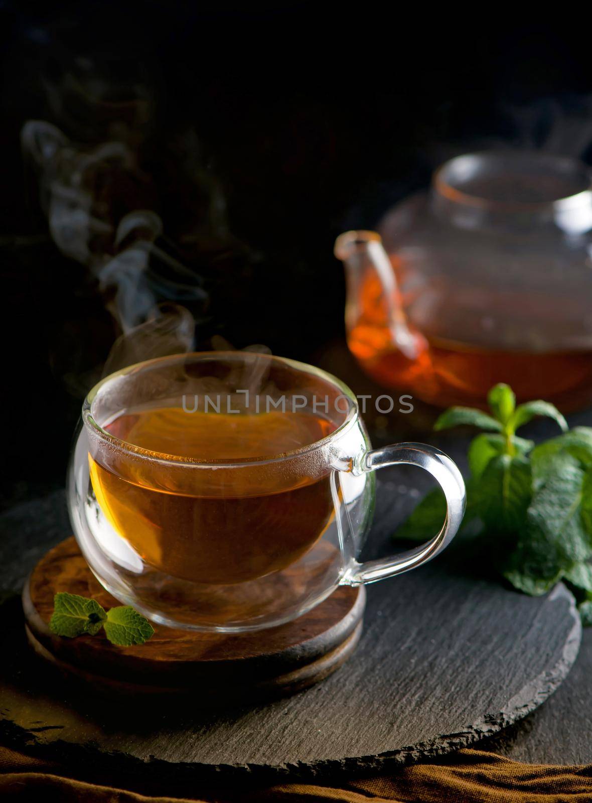 Teapot with tea surrounded with green leaves, tea ceremony, green tea in a transparent cup