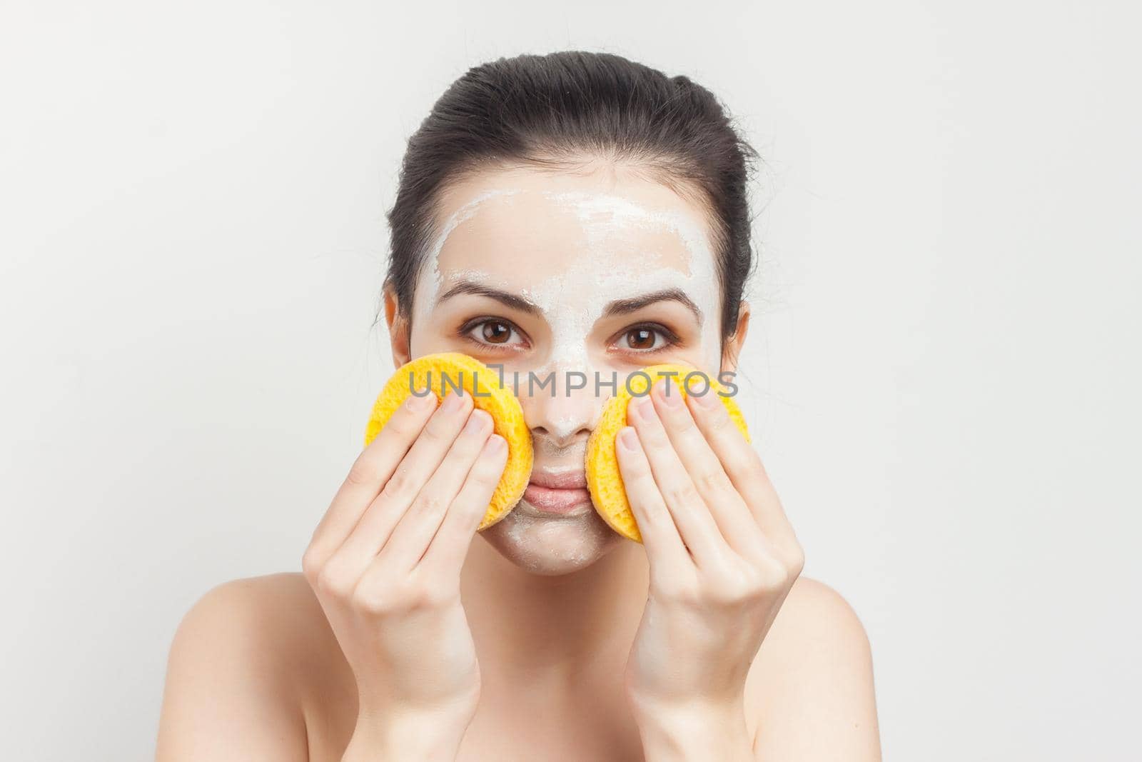 woman with bare shoulders wipes a mask on her face with sponges. High quality photo