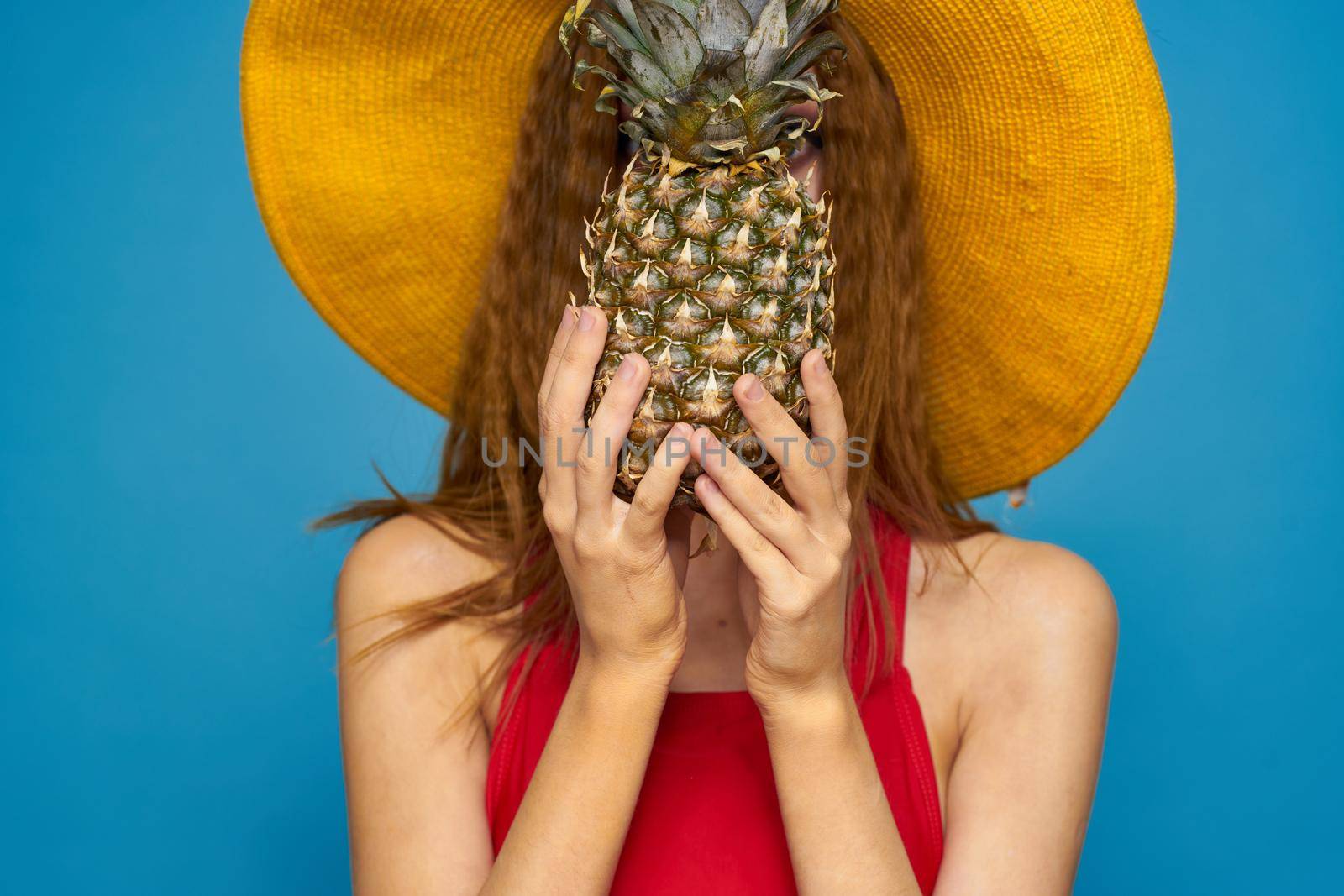 Woman in yellow hat with pineapple in hands emotions fun lifestyle summer fruit blue background. High quality photo