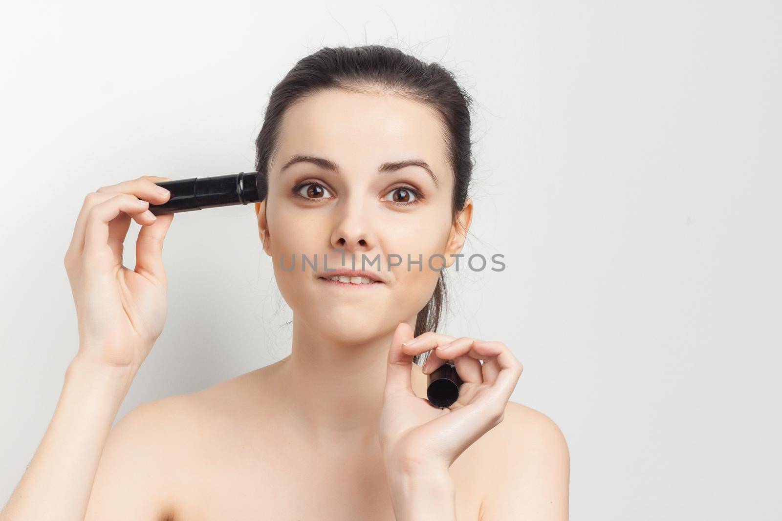 pretty woman applying makeup brush on face skin care naked shoulders. High quality photo