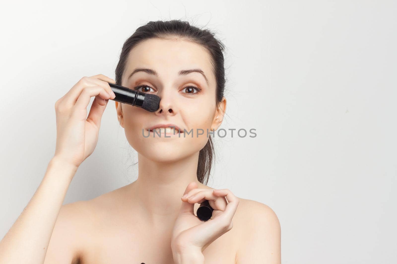 attractive brunette with cream on her face brush in hands applying makeup. High quality photo