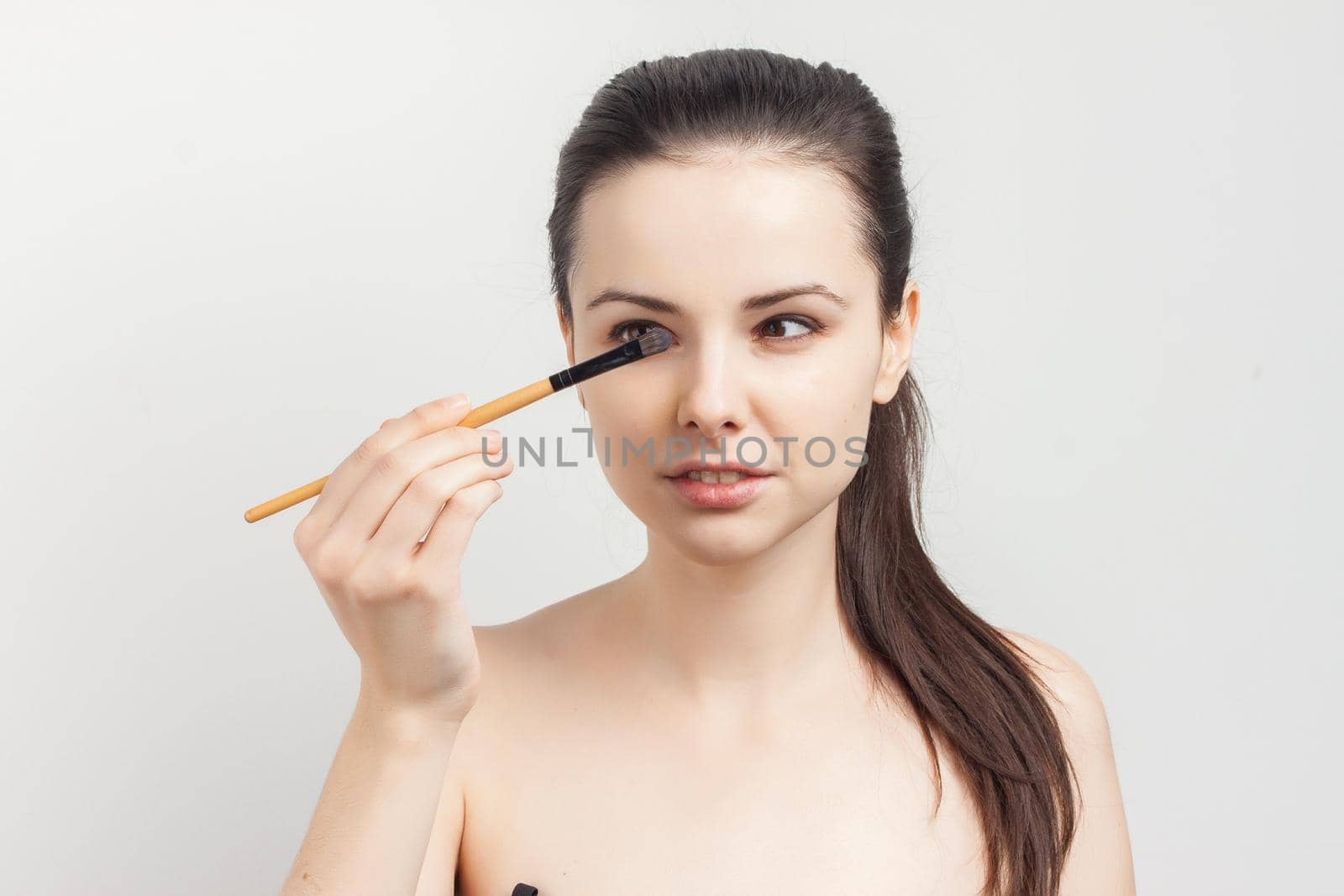 cute bare-shouldered brunette applying makeup on face cropped view. High quality photo