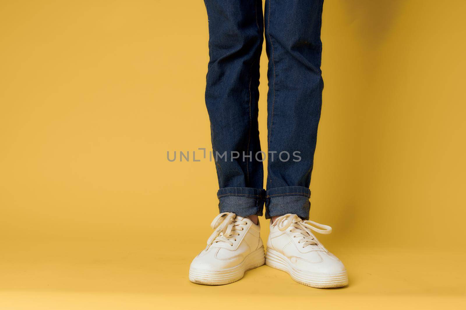 feet jeans fashion shoes white sneakers yellow background. High quality photo