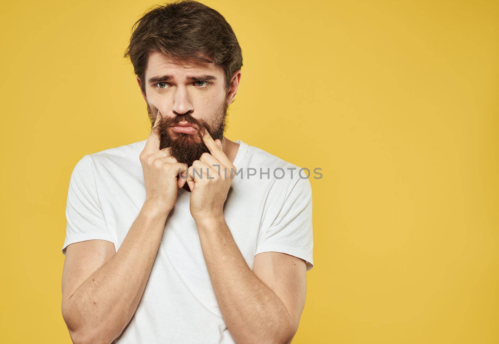 A man in a white t-shirt gestures with his hands on a yellow background cropped view. High quality photo