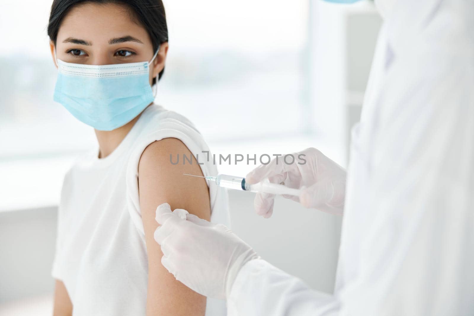 doctor in protective gloves makes an injection in the shoulder woman in a medical mask covid vaccination by SHOTPRIME