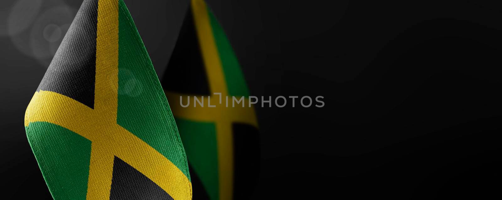 Small national flags of the Jamaica on a dark background.