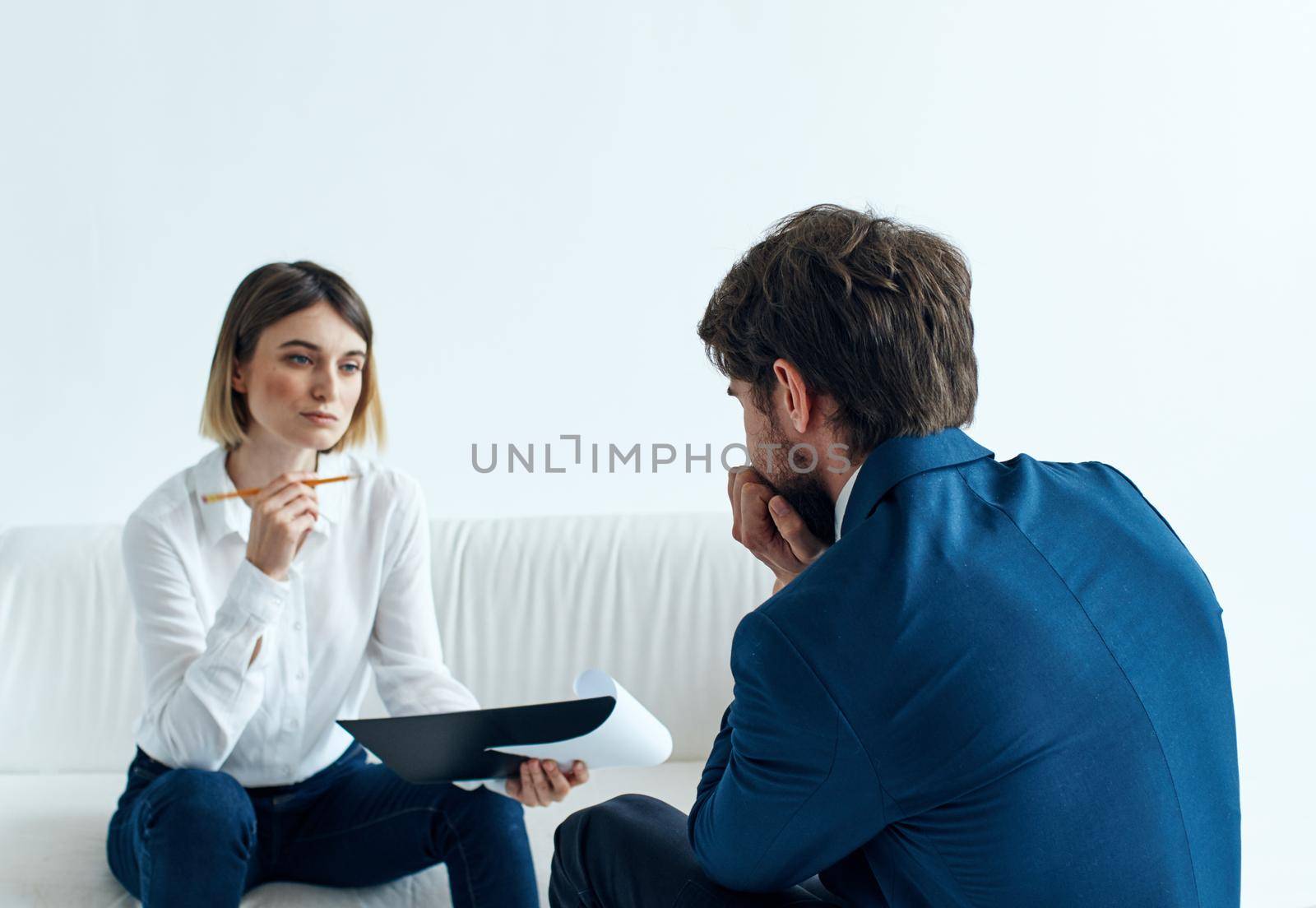 A business man in a suit is gesturing with his hands and a woman is sitting on the couch. High quality photo