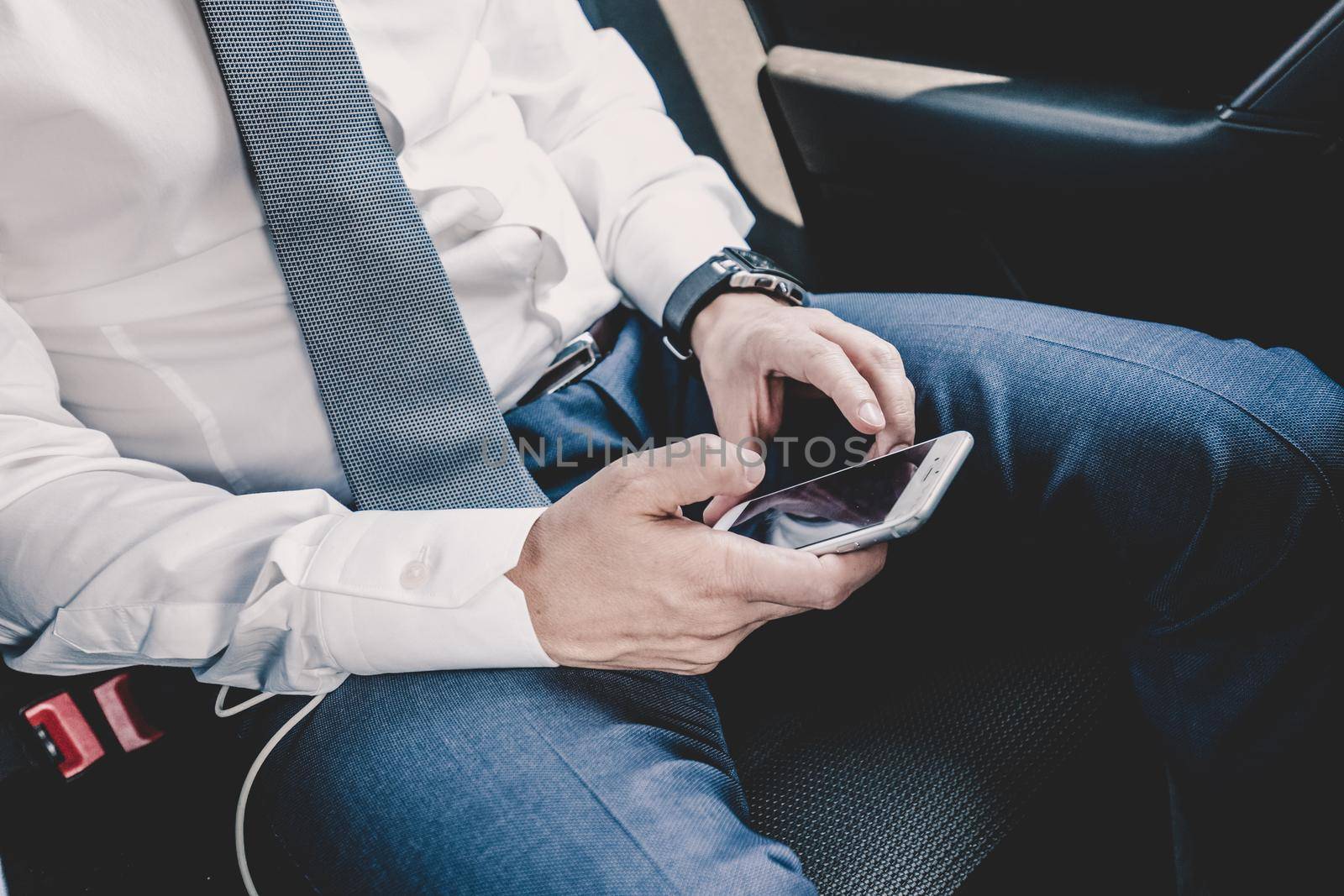 Close up of a businessman using smart phone while driving on the back seat of a car. Focus on mobile device.