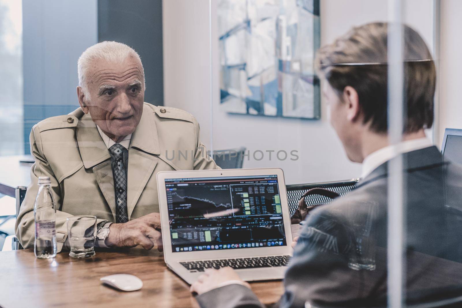 Young financial advisor sitting in front of laptop, consulting senior client with his investment strategy.