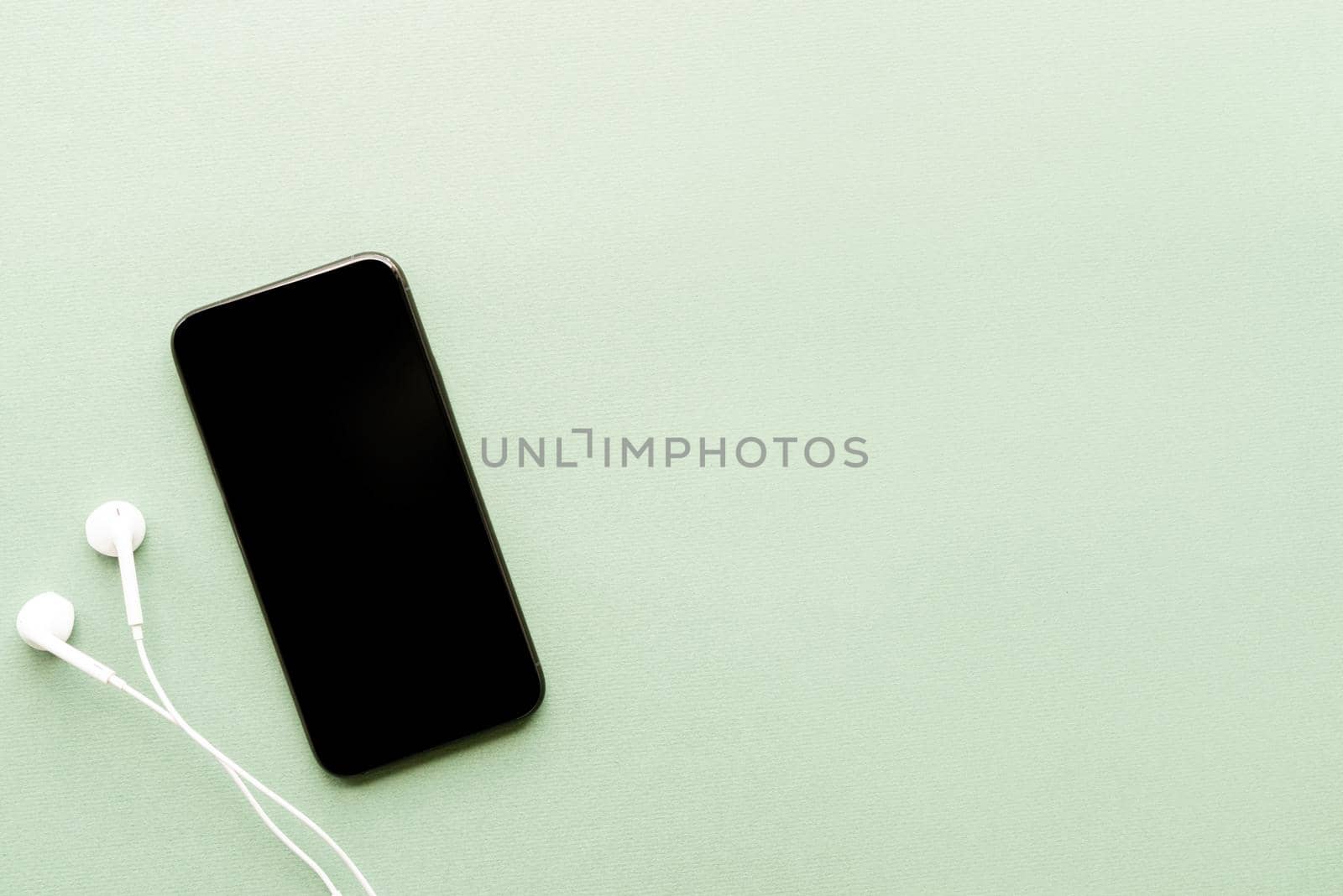 top view of smartphone with blank screen headphones on green background by Desperada