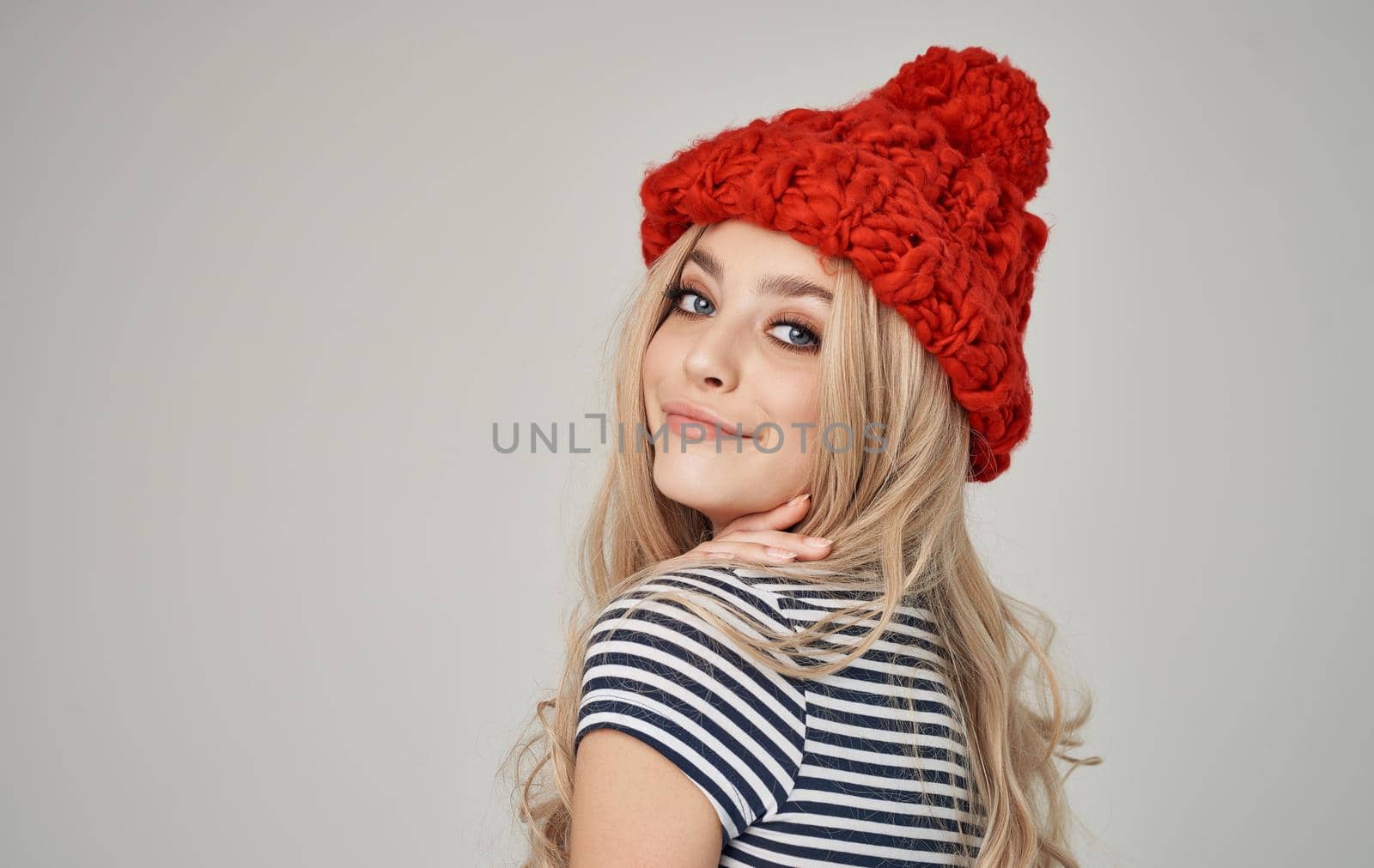beautiful blonde in a warm hat and striped T-shirt on a light background. High quality photo