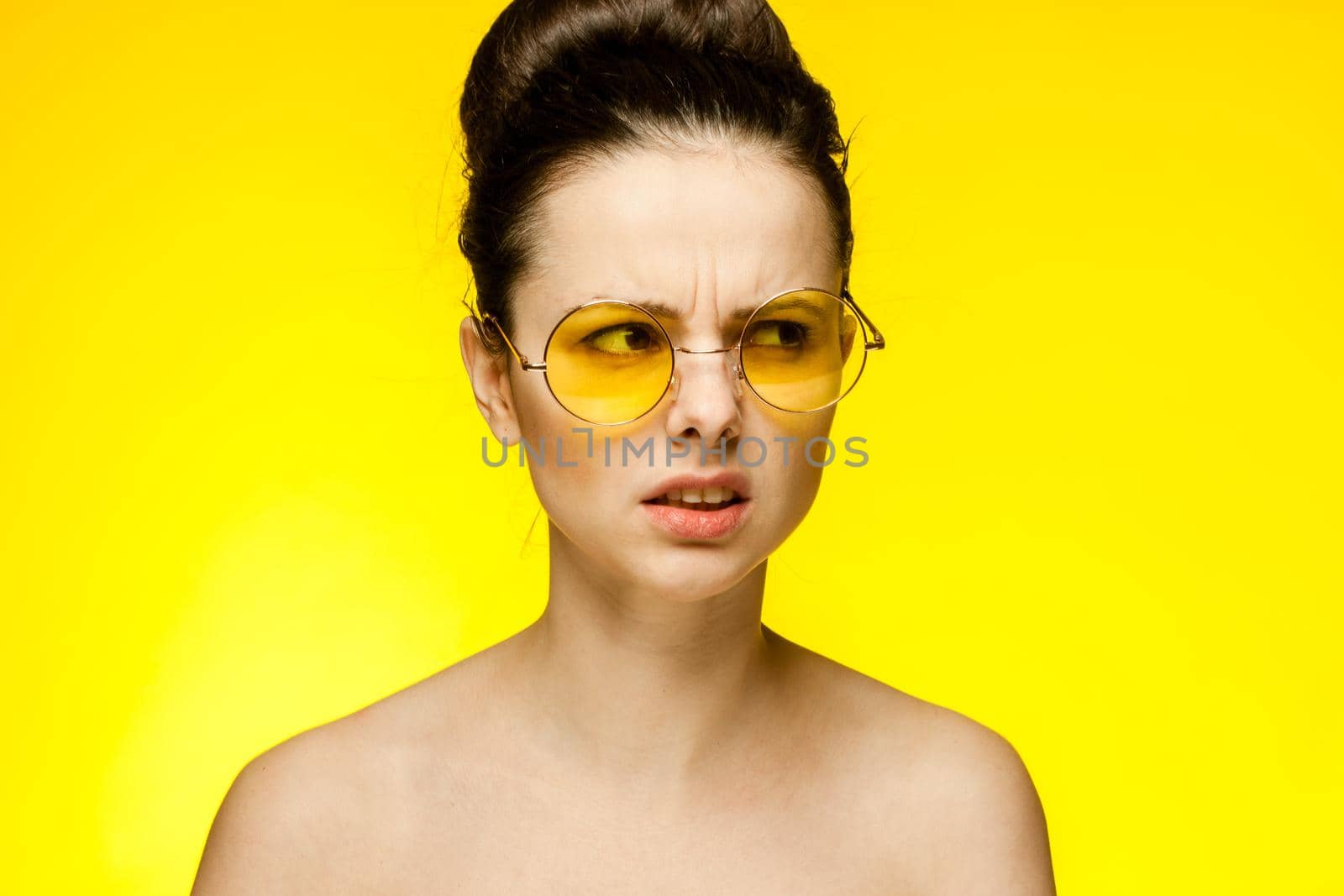 emotional woman with bare shoulders wearing fashion glasses gathered hair yellow background. High quality photo